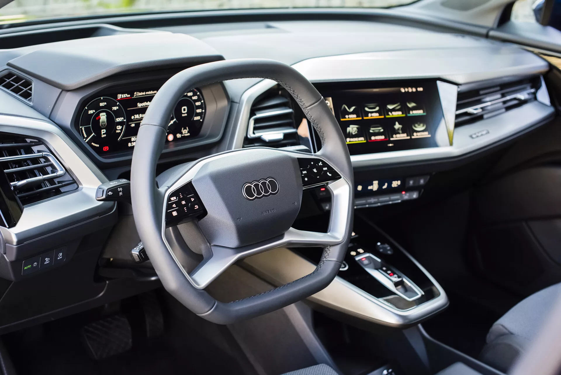 2021-es Audi Q4 e-tron belső nézet a vezető oldaláról, bemutatva egy multifunkcionális kormánykereket Audi logóval, digitális műszerfalat, középkonzolt sebességváltóval, érintésre érzékeny HVAC vezérlőkkel, infotainment kijelzővel, elegáns műszerfallal integrált légbeömlőkkel, és luxus bőrrel bélelt ajtóval, amely modern autótechnológiát és luxusjármű funkciókat mutat be.