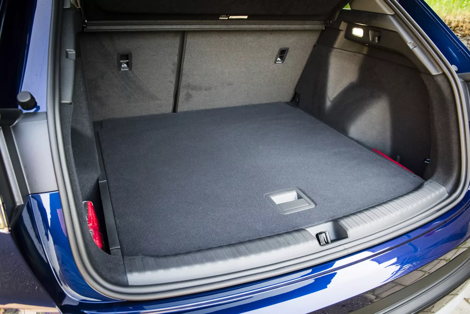 Az Audi Q4 e-tron 2021 tágas, szőnyegezett csomagtartójának nézete az open csomagtartó fedéllel, okos tárolási megoldásokat és a fémes kék külsőt és a látható parkolóérzékelőt mutatva