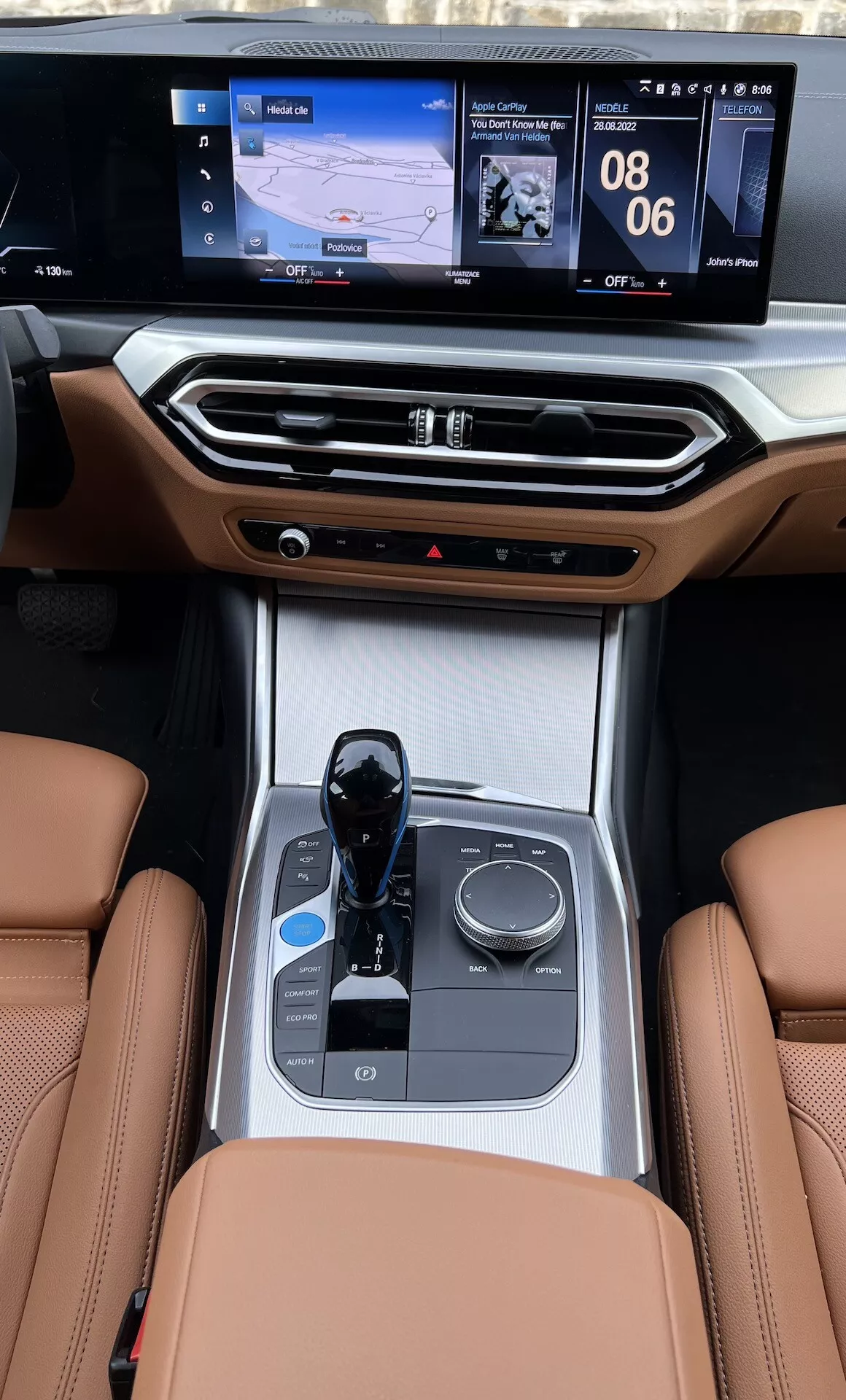 A 2021-es BMW i4 belső középkonzoljának nézete a hátsó ülésekről, kiemelve a bőr üléseket, az elektronikus váltókar, a multimédia vezérlőgomb, a pohártartók, a klímavezérlések és a dupla interfészes infotainment képernyőt navigációs és média kijelzőkkel