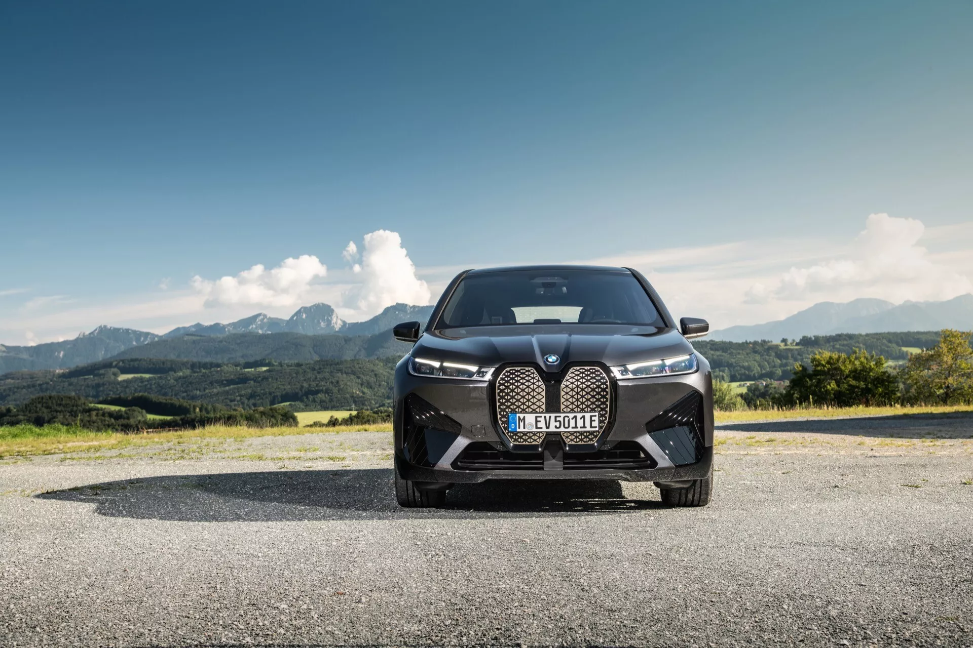 2021-es BMW iX (i20) fényképezve az elejéről alacsony szögből, kiemelve az uralkodó tervezést egy nagy vesemedence-ráccsal, elegáns LED-es fényszórókkal és teljesítmény-orientált légbeömlőkkel hegyvidéki táj előterében