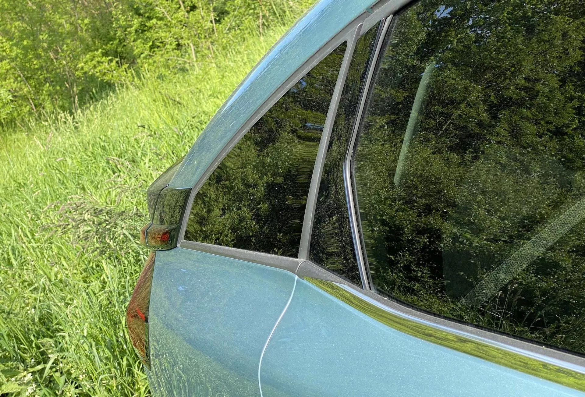 Közelről készült kép a Citroen C4 2020 (e-C4) hátsó negyedpaneljéről és ablakáról. A felvétel egy ferde szögből készült a jármű hátsó oldalánál, kiemelve az átmenetet a hátsó utasablaktól a hátsó szélvédőig. Látható a fémes világoskék festék, a C-oszlopon lévő narancssárga oldaljelző lámpa, a krómozott díszítés és az üvegfelületek csillogása, kiemelve az autó formatervezését és állapotát.