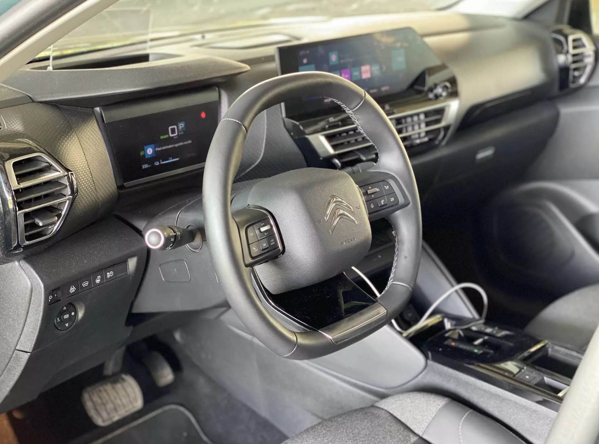 2020-as Citroën e-C4 belső látkép az első ülés utasának nézőpontjából, amely magába foglalja a vezetőülést, a középkonzolt, a beépített vezérlőgombokkal ellátott kormánykereket, a digitális műszerfalat és a központi szórakoztató kijelzőt. A műszerfal geometriai kialakítású, sötét és világos anyagokkal. A középkonzol fizikai klímaszabályzókat és automata sebességváltót tartalmaz.