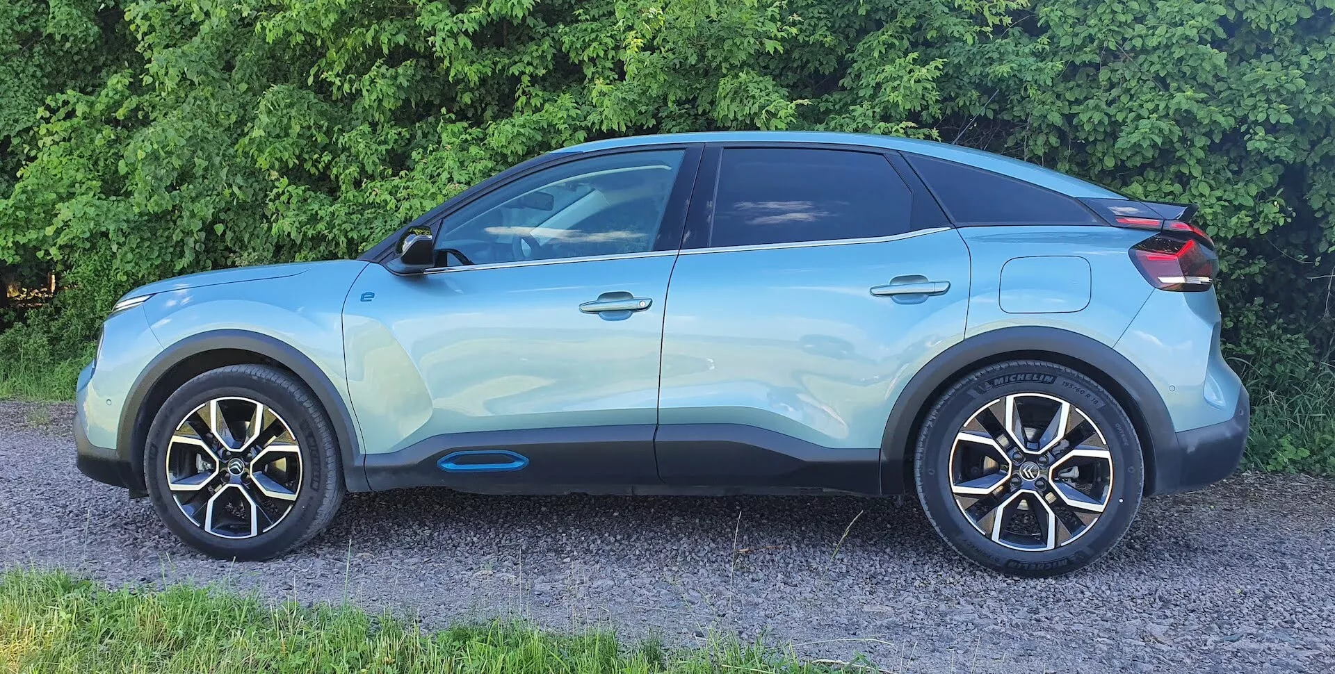 Egy 2020-as Citroen C4 (e-C4) modern crossover SUV oldalnézeti profilja. A világoskék jármű egy oldal-elülső szögből lett fényképezve, kiemelve olyan részleteket, mint a fényes felület, a könnyűfém keréktárcsák, a karosszéria színével megegyező oldalsó tükrök, a merész karaktervonalak, a fekete ablakkeretek, az elsötétített hátsó ablakok, a süllyesztett kilincsek kulcs nélküli bejutással és a hátrafelé dőlő tetővonal lehetséges légterelővel és tetősínekkel. A kép jól láthatóan mutatja az első kereket és sárvédőt, de a hűtőrács, a lökhárító és a fényszórók nem látszanak.