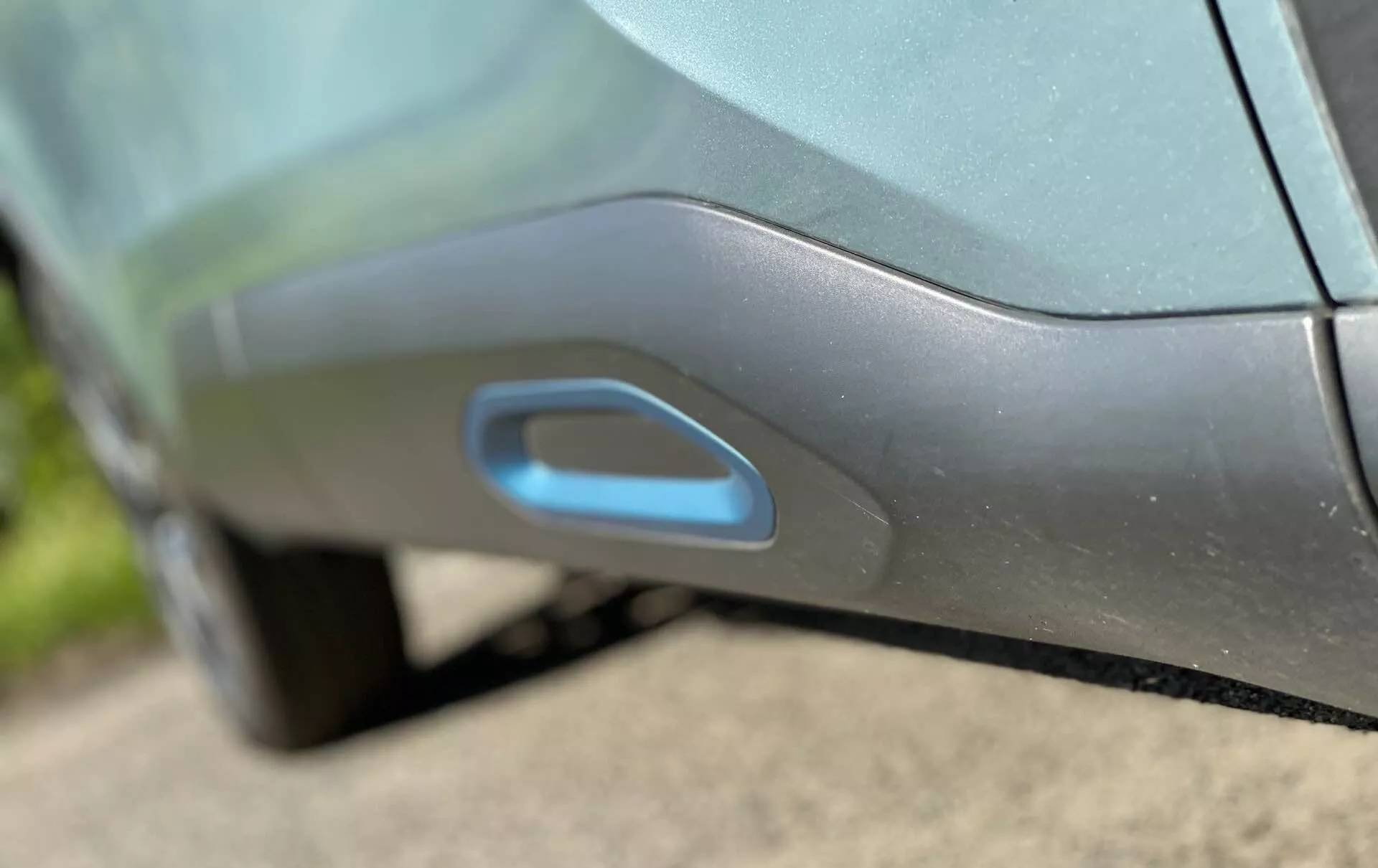 Közelkép a Citroen C4 2020 (e-C4) oldalának részletéről, amely kiemeli a modern, aerodinamikailag integrált ajtókilincset. A kilincs egy síkban van az ajtópanellel, esetleg megvilágított a kulcs nélküli bejutáshoz, amely fejlett elektronikus csúszó vagy kiugró mechanizmusra utal. Az autó metálszínét és fényes felületét a nappali fény és tükröződések hangsúlyozzák.