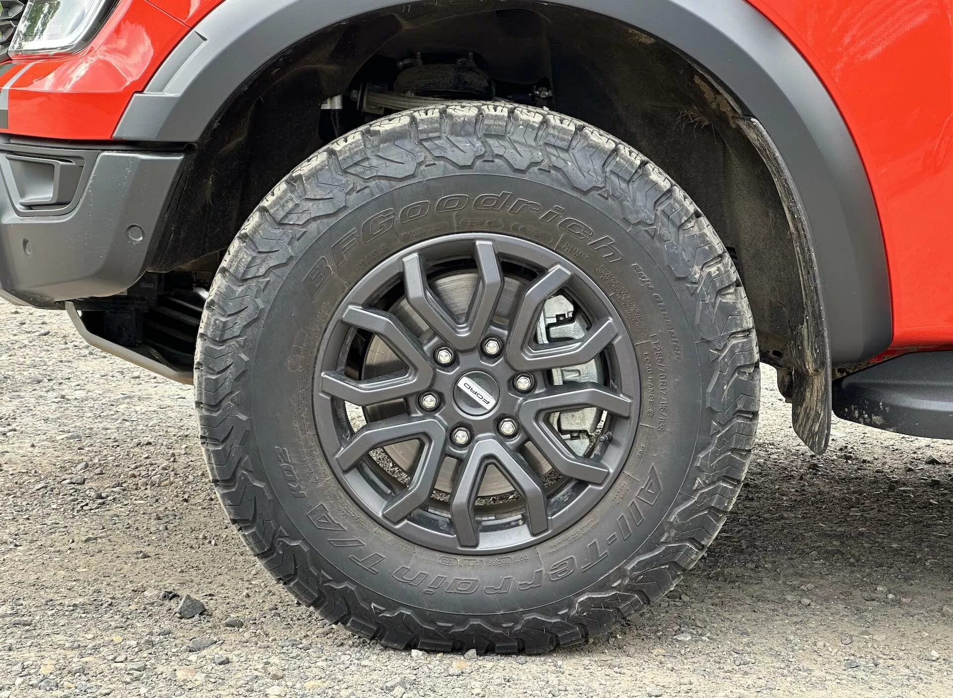 2022-es Ford Ranger kerék közelképe, amely többszórt spriccelt ötvözeti kialakítást, minden terepre alkalmas abroncsmintát és a sárvédő egy részét mutatja, látható a felfüggesztés emelkedése