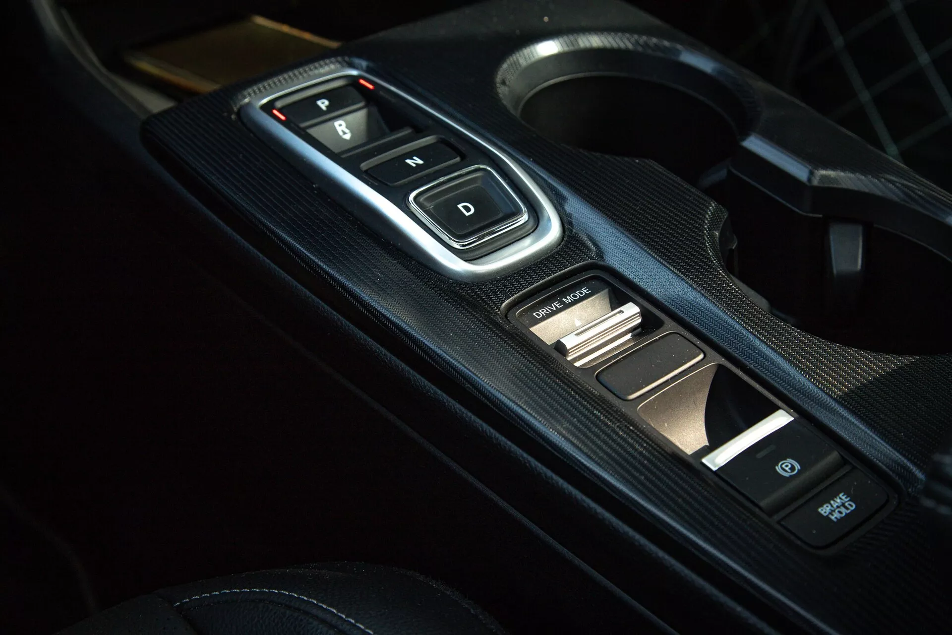 2022-es Honda Civic belső részlete a középkonzolon, elektronikus váltóválasztóval 'P, R, N, D' gombokkal, szén-szál mintás panellel és kiegészítő vezérlőkkel, modern automata váltót és sportos esztétikát bemutató