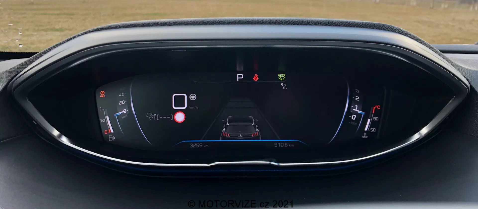 A Peugeot 5008 2021 műszerfala, digitális kijelzővel a vezetőülés perspektívájából. A kijelző tartalmaz egy teljesítmény/akkumulátor mérőt, egy központi autó grafikát figyelmeztető ikonokkal, egy 'P' parkolás jelzőt, egy üzemanyag-mérőt és a kilométeróra/útinformációkat. A dizájn modern, kék és piros színsémát követ elegáns, ívelt házzal. Vízjel © MOTOR1ZED 2021.