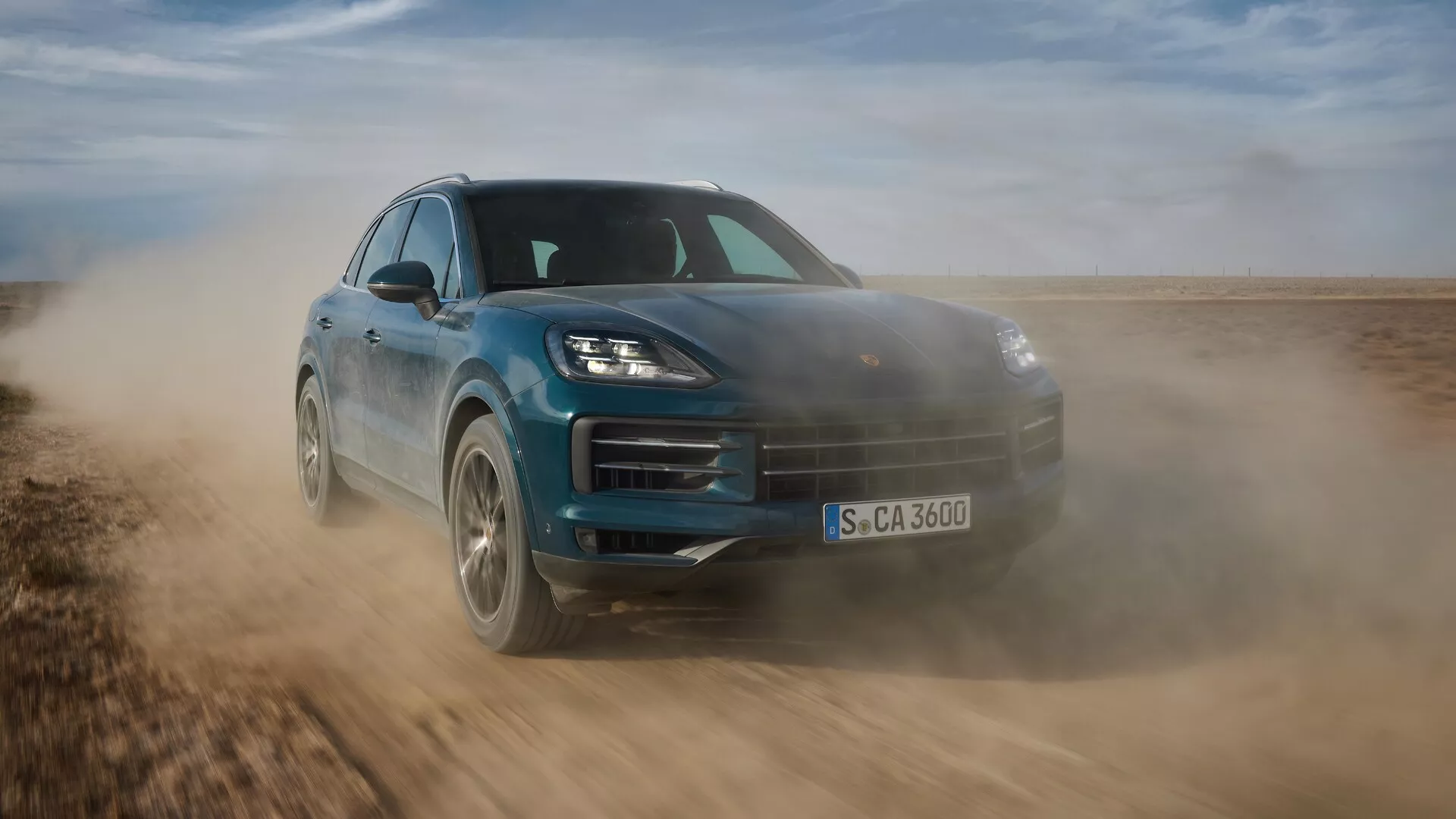 2023-as Porsche Cayenne (9YA modellfrissítés) dinamikus mozgásban, bemutatva karcsú tervezését és terepjáró képességeit, alacsony első háromnegyed nézetből készült felvétellel, kiemelve a sportos tartást, fejlett LED fényszórókat és aerodinamikai jellemzőket nem aszfaltozott felületen.