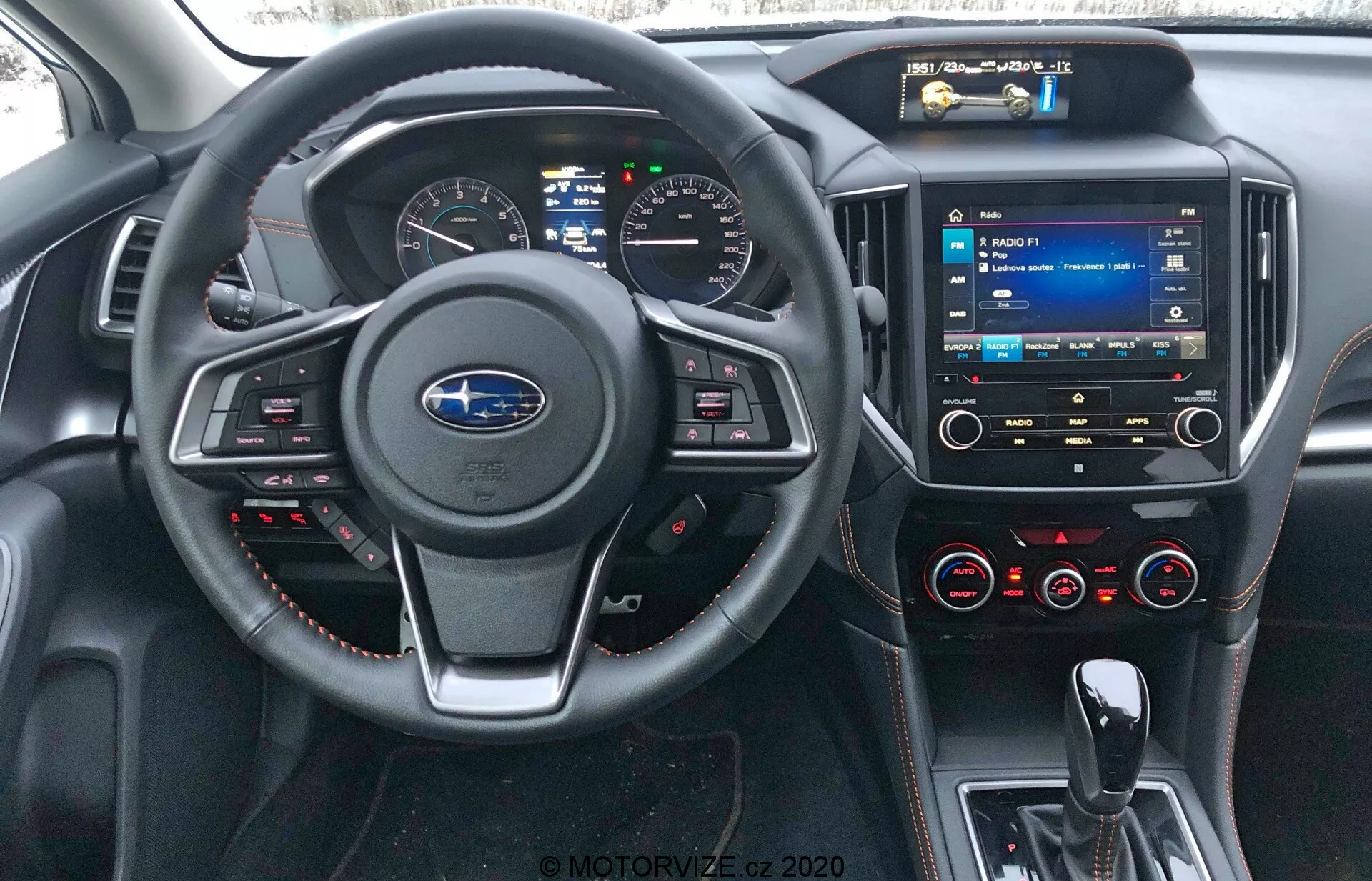 Subaru XV 2018 belső nézete a vezetőülés szemszögéből, amelyen látható a Subaru logó kormánykeréken vezérlőgombokkal, piros varrás részlettel, digitális műszerfal, középkonzolon érintőképernyős multimédia rendszer, klíma szabályozó gombok, USB portok, 3,5 mm-es audio bemenet és bőrszerű anyagok piros varrással a műszerfalon és az ajtópanelen.