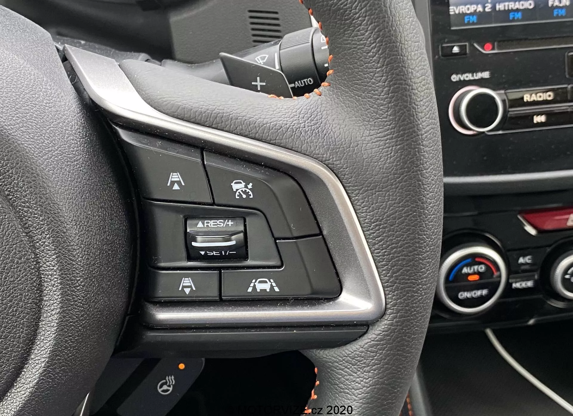 Közelkép egy 2018-as Subaru XV kormányának bal oldali vezérlőiről, amelyek Adaptív Sebességtartó Automatával, Sebességkorlátozóval, Hangvezérlés gombbal és Sávtartó Asszisztenssel vannak felszerelve. A kép a vezető ülésből készült, kiemelve a fekete műanyag felületen lévő megvilágított szimbólumokat, a műszerfal és a középkonzol részletei láthatóak a háttérben.