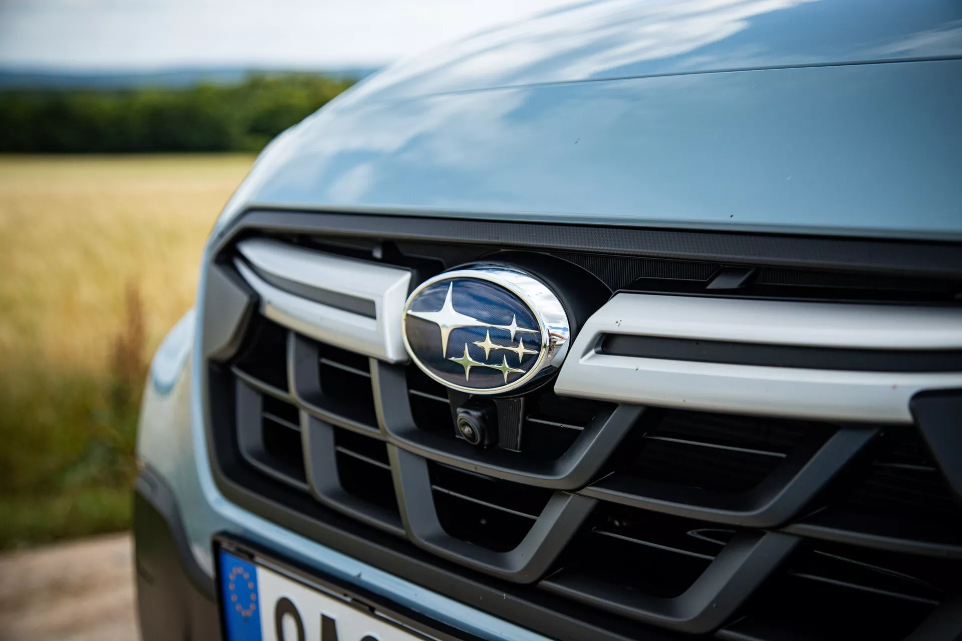 A 2021-es Subaru XV első hűtőrácsának és emblémájának közeli nézete, amely fémes vízszintes lamelláit mutatja be, sötét árnyalatban, a jelvényre összpontosító sekély mélységélességgel, ami luxus autójellemzőket sejtet.