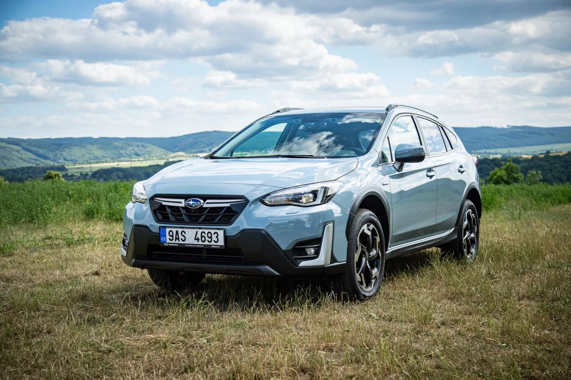 2021-es Subaru XV crossover SUV parkol a füvön dombos háttérrel, kiemelve az első homlokzatot, az oldalprofilot és a keréktervezést