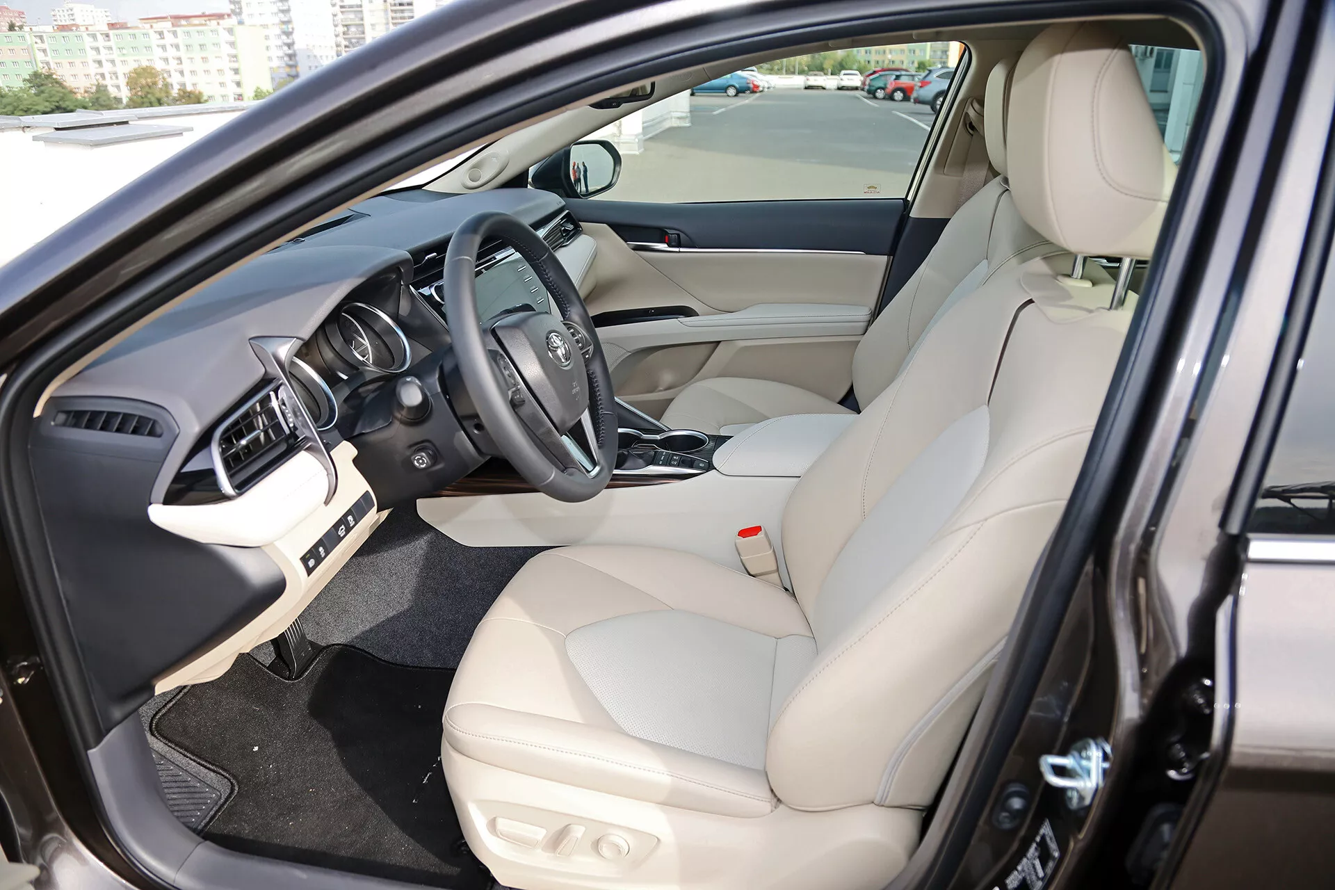 2001-es Toyota Camry Limuzin belső terének megjelenítése az autó vezetői területéről ferde előlről nézetből nyitott ajtóval, kiemelve az elektronikus vezérlőkkel ellátott bőrüléses vezetői ülést, a gyártó logójával és szerelt vezérlőkkel ellátott központi kormánykereket, a műszerfalat infotainment képernyővel, és az elektromos ablakok vezérlésével ellátott belső ajtópanelt.