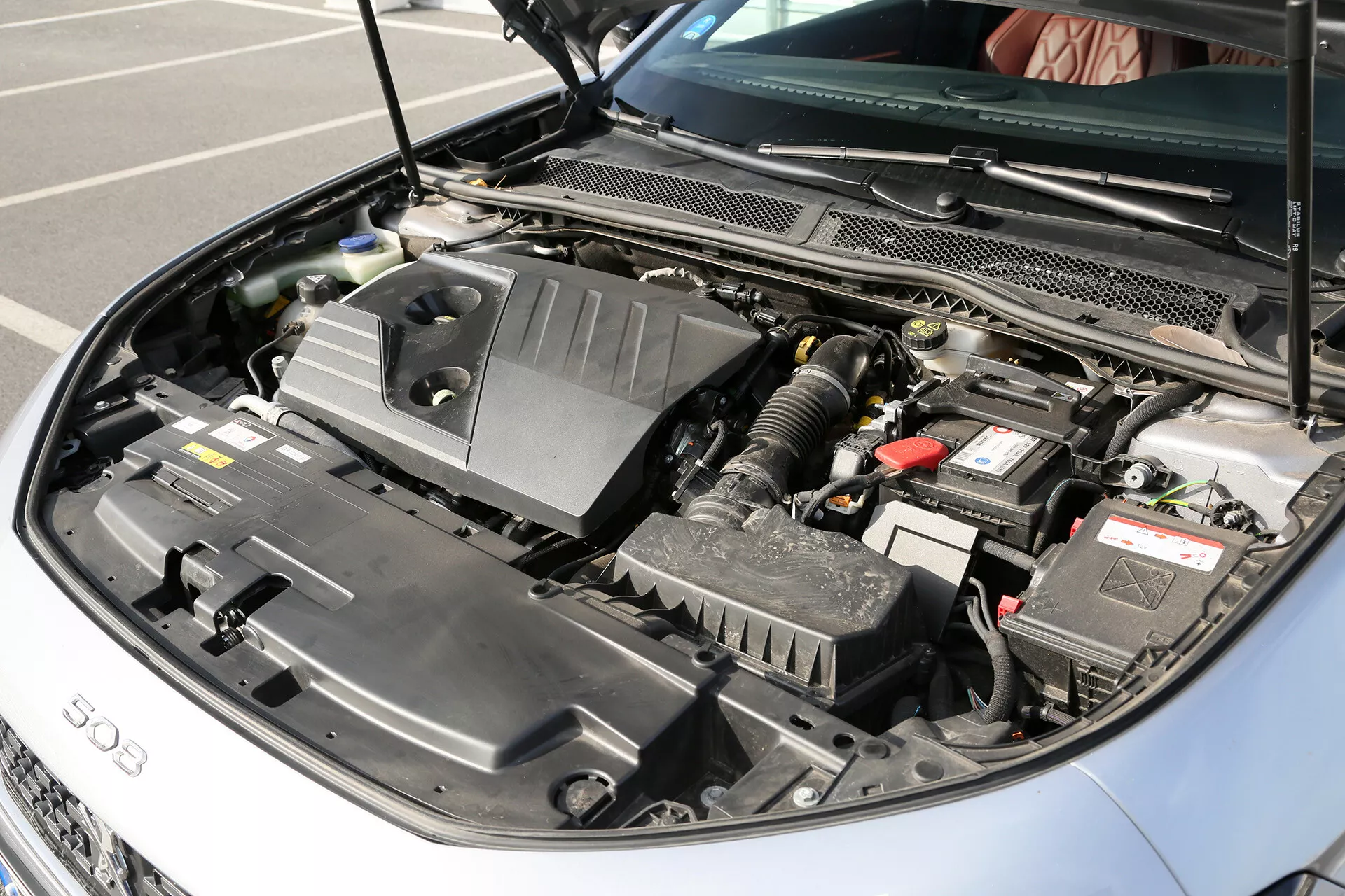 Közeli nézet a 2001-es Toyota Camry (Camry Limuzin) nyitott motoros részére, bemutatva a '500' feliratú motorborítót, autó akkumulátort, légszűrő dobozt, folyadéktartályokat, összetett kábelezést és csövezést, a borító alatt látható motoralkatrészeket és a hűtőrácsot, kiemelve a jármű modern belső égésű motor technológiáját.