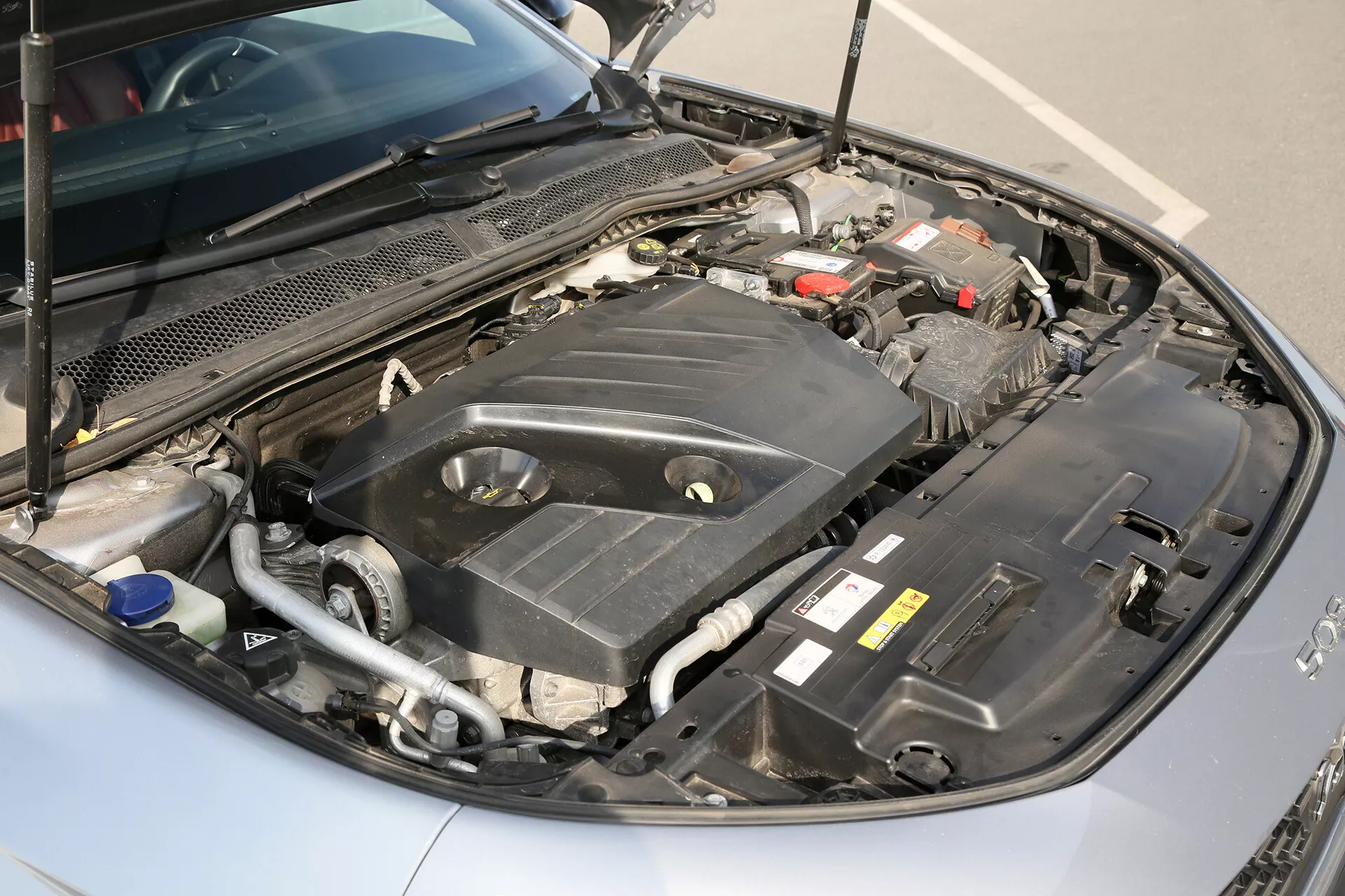 Közeli nézet egy 2001-es Toyota Camry Limuzin nyitott motoros részére, kiemelve a motorborítást, az autó akkumulátorát, a folyadéktartályokat, a csöveket és a motor komponenseit egy közepes- magas szögből.