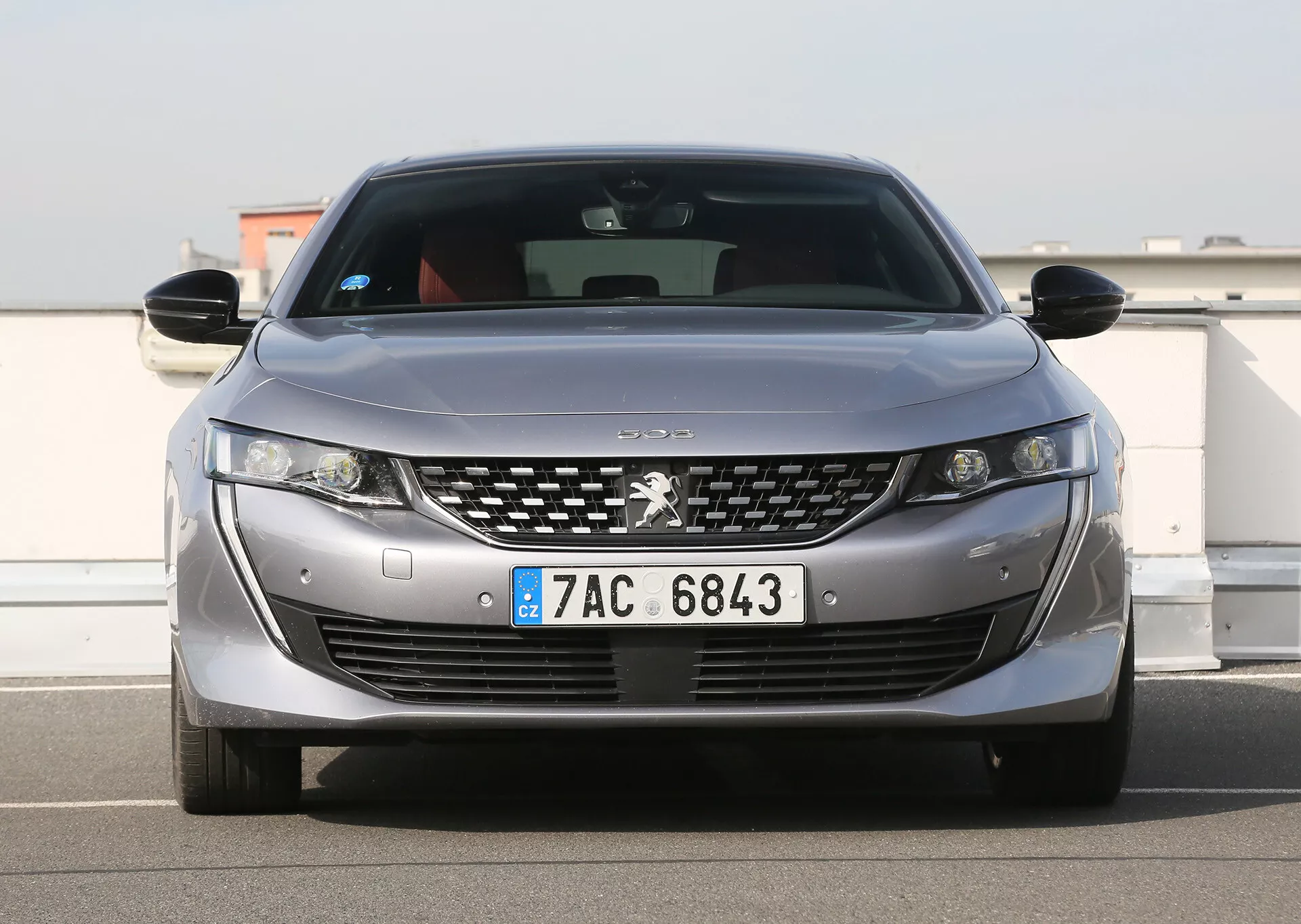 Ezüstszínű Peugeot első nézete LED fényszórókkal, krómozott részletekkel díszített hűtőráccsal, parkoló szenzorokkal és európai rendszámtáblával, amely a modern design és technológiai jellemzőket mutatja be, szabadtéren parkolva tiszta égbolt alatt