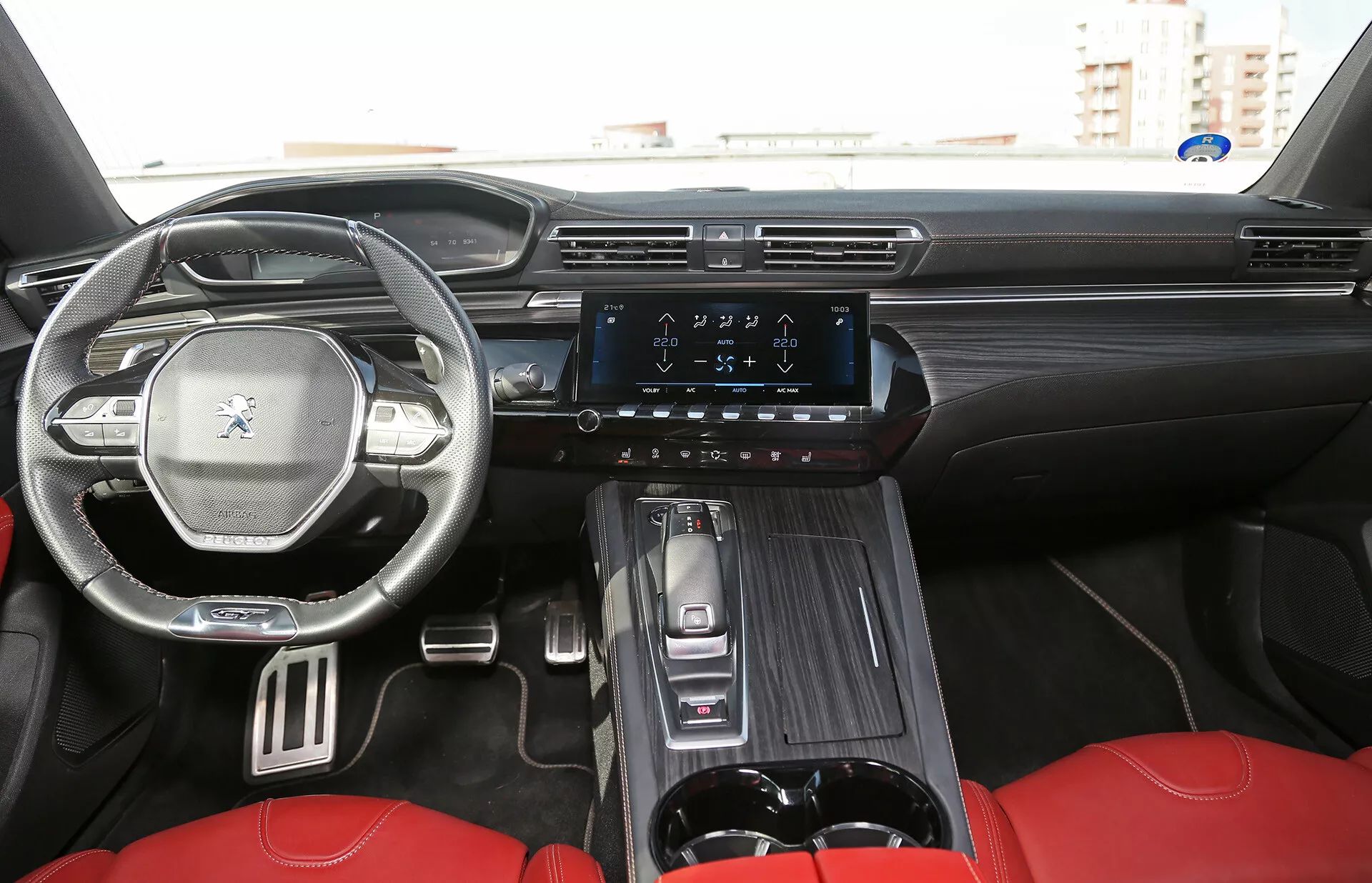 A 2001-es Toyota Camry Limousine belsejének nézete, ahol a műszerfal, a vezérlőgombokkal ellátott kormánykerék, a digitális kijelző, a függőleges érintőképernyős infotainment rendszer és a luxus piros ülések láthatók az első kabinban, a hátsó ülésből nézve