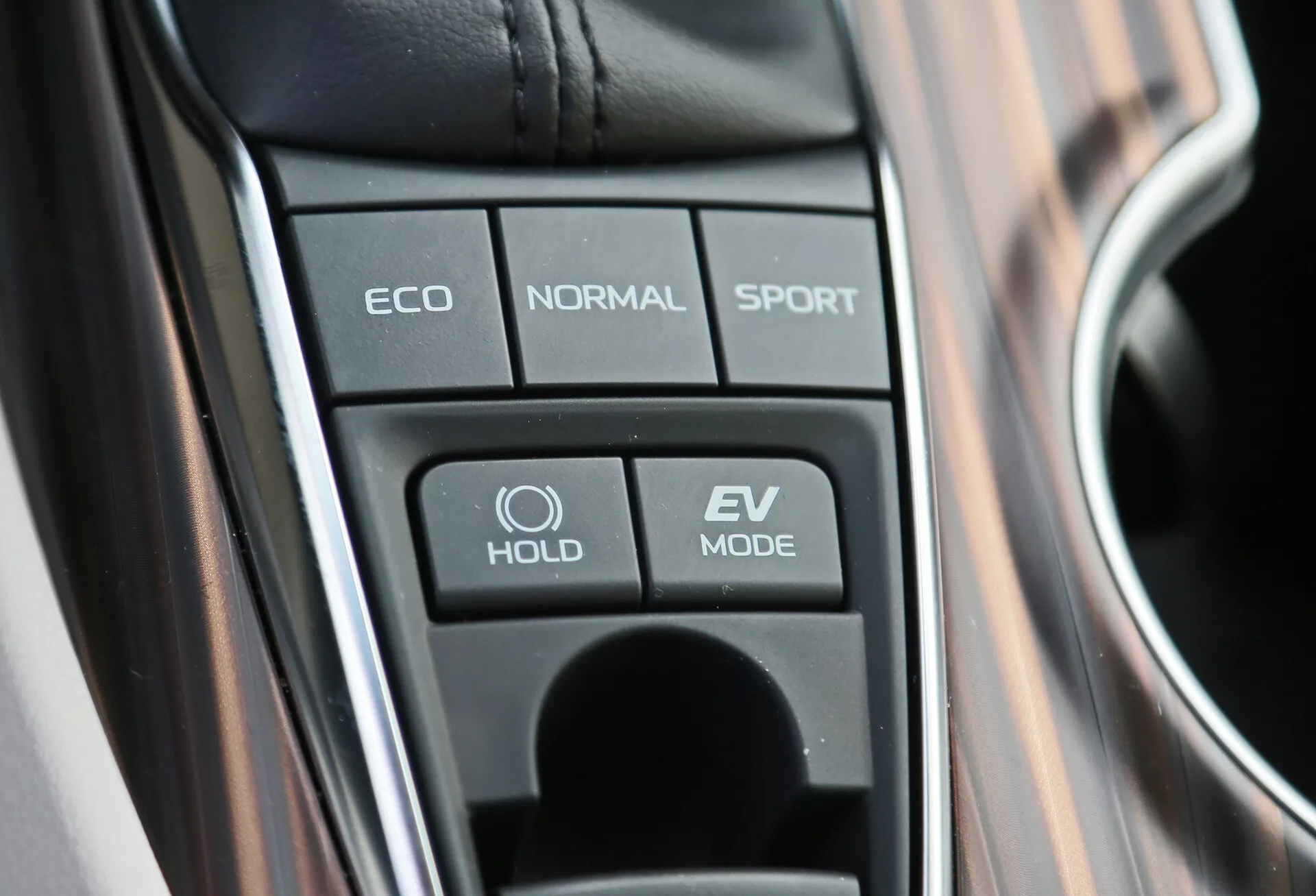 Közeli nézet a Toyota Camry 2001 középkonzoljára, amely a meghajtási mód kiválasztás gombjait tartalmazza, beleértve az ECO, NORMAL, SPORT, HOLD funkciót és az EV MODE-ot, kiemelve a fejlett járműtechnológiákat és a hibrid képességeket.