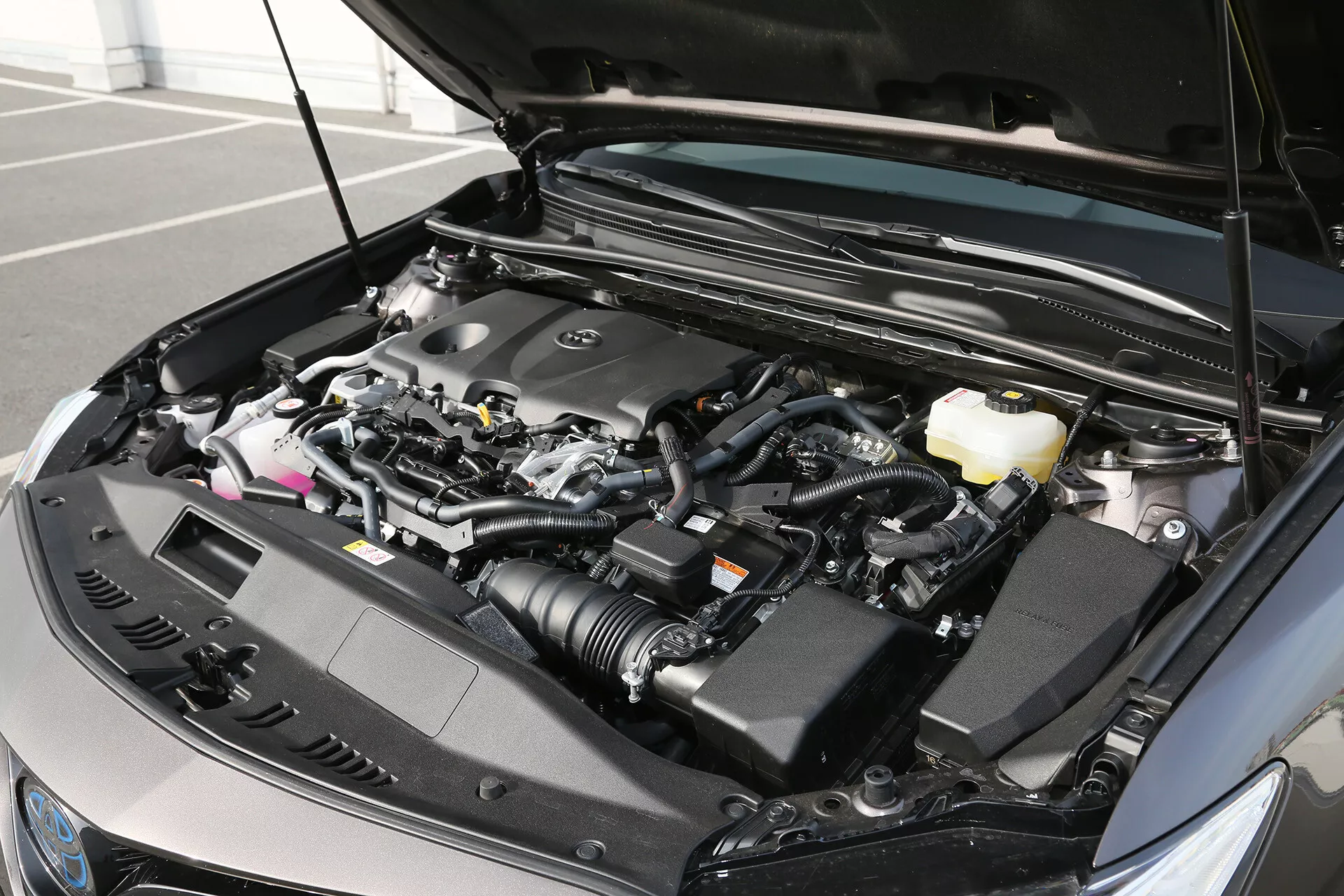 Részletes nézet egy 2001-es Toyota Camry Limousine motorházára az elől háromnegyedes szögből, bemutatva a motorblokkot, a levegőbevezető tömlőt, a folyadéktartályokat, a vezetékkötegeket és a védőelemeket, egyenletes megvilágítással jelezve a nappali vagy külső világítást.