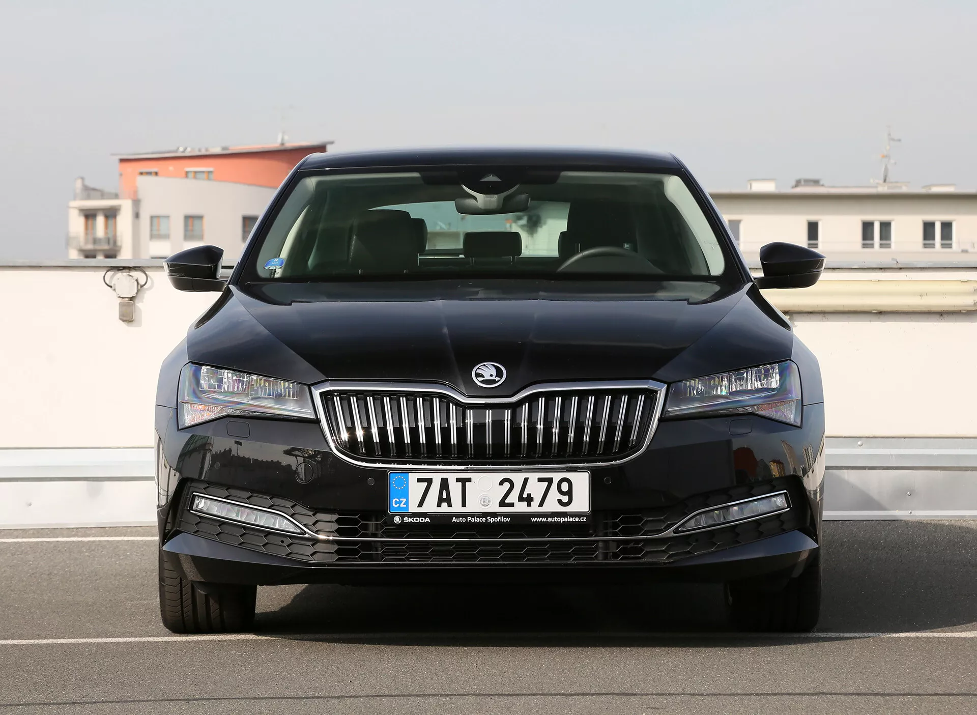 Fekete Škoda szedán első nézete LED fényszórókkal, nappali menetfényekkel, króm függőleges lamellás ráccsal központi Škoda jelvényvel, integrált ködlámpákkal a lökhárítón, és a Cseh Köztársaságban regisztrált látható első rendszámtáblával