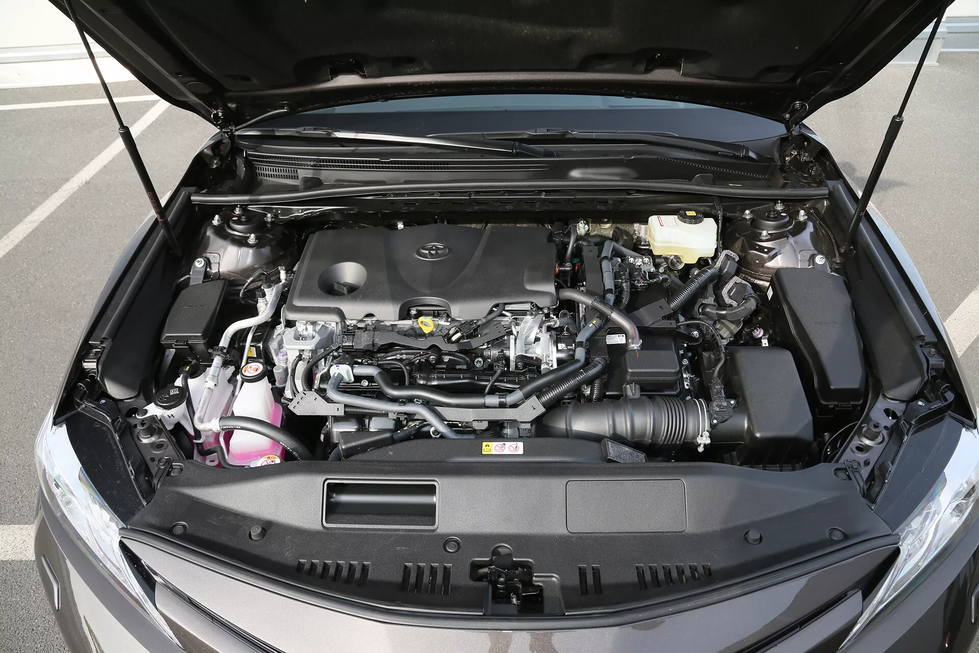 Részletes nézet egy 2001-es Toyota Camry limuzin motoros részéről, nyitott motorháztetővel, bemutatva a modern autómotor tervezést, látható légszívó tömlőt, fékfolyadék-tartályt, elektronikus kábelezést és a hűtőrendszer elemeit