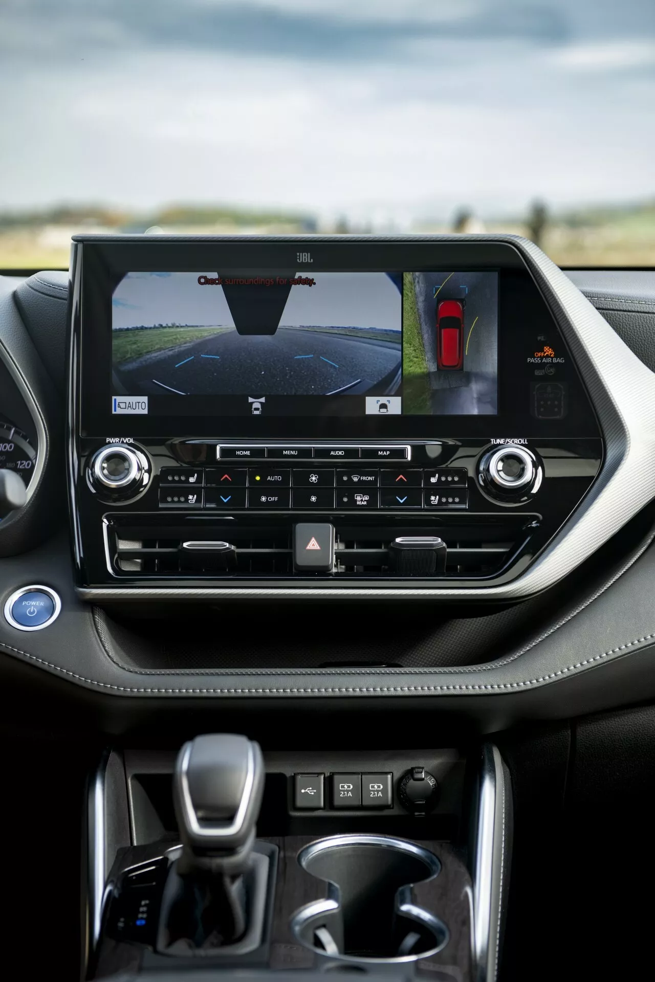 2021-es Toyota Highlander belső tere kiemelve a középkonzolt tájkép-orientált érintőképernyővel, amelyik a hátsó nézetű kamerát és parkoló segítséget mutat, kétzónás klímavezérlőkkel és automata váltóval