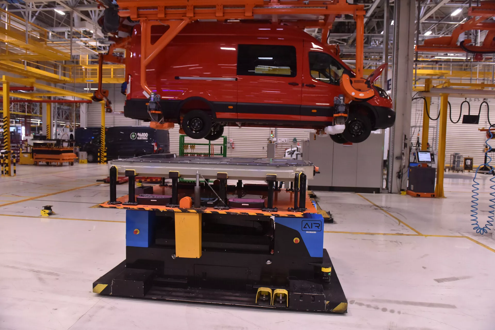 2017-es Alfa Romeo Stelvio élénk piros színben, daruval felfüggesztve ipari gyári környezetben, bemutatva a jármű összeszerelési folyamatát oldalnézeti és hátsó negyednézeti képpel