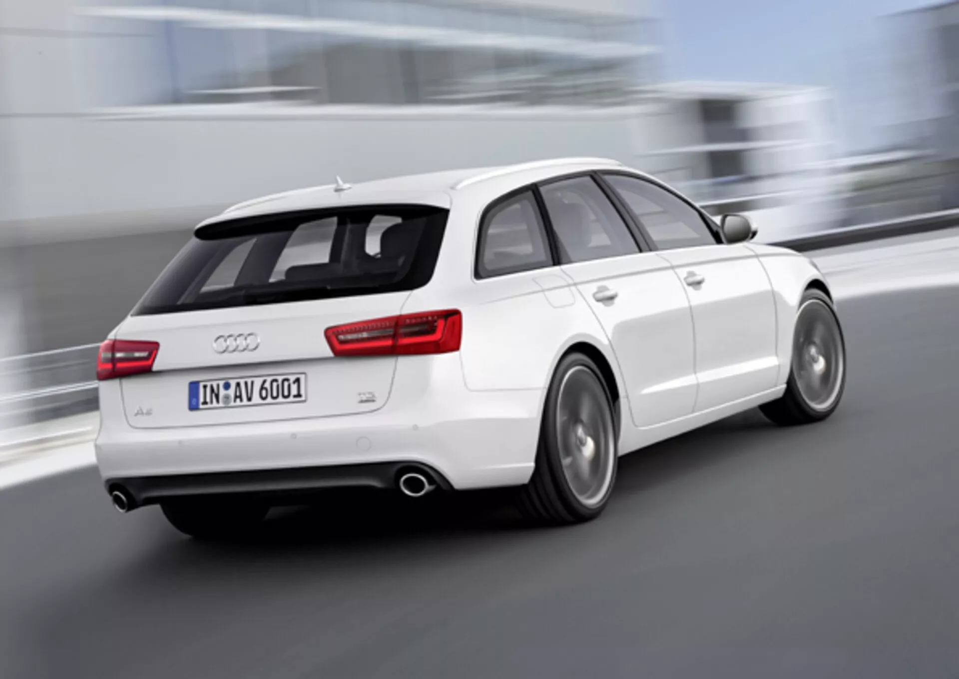 Dinamikus háromnegyedes hátsó nézetű fehér 2011-es Audi A6 Avant mozgásban, elmosódott kerekekkel, amelyek a sebességet jeleznek, kettős kipufogóval, ötvözött keréktárcsákkal, amelyeknél láthatóak a féktárcsák, és tetőn elhelyezett spoilerrel a jobb aerodinamikáért, kültéren készült.