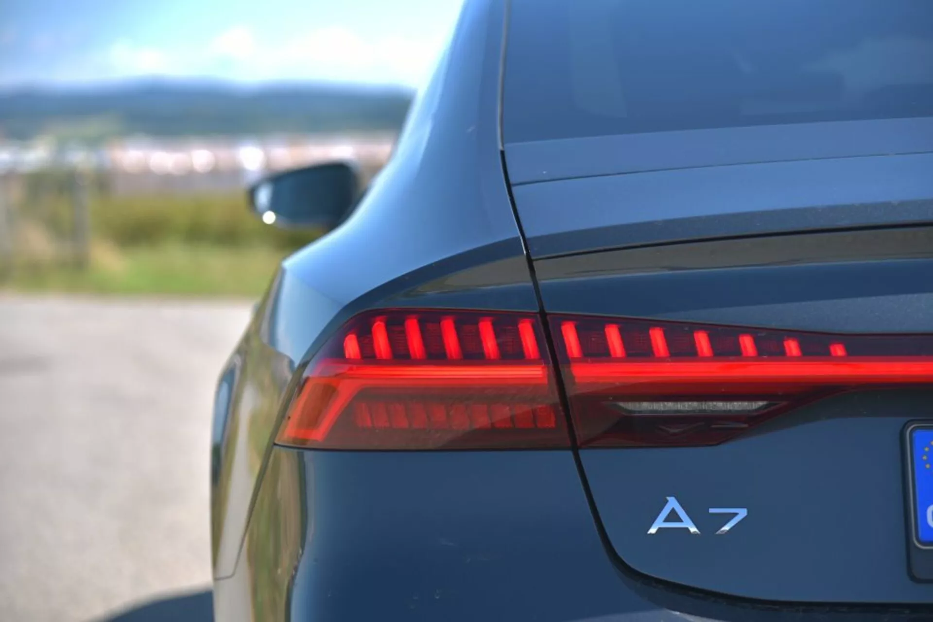 Közelkép az elsötétített LED hátsó lámpáról és az A7 jelzésről a sötétkék Audi A7 Sportback hátsó oldalán, kiemelve a modern autótervezés jellemzőit és a luxus részleteket