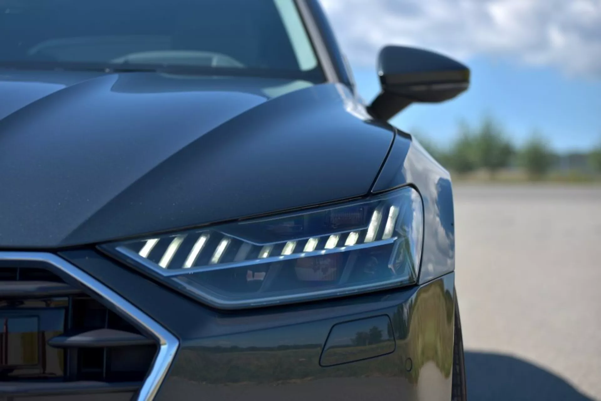 2018-as Audi A7 Sportback közelképe, kiemelve a LED fényszóró tervezését, a részben látható hűtőrácsot és az aerodinamikus vonalakat alacsony szögből, bemutatva a modern luxusautó jellemzőit és a fejlett világítástechnológiát