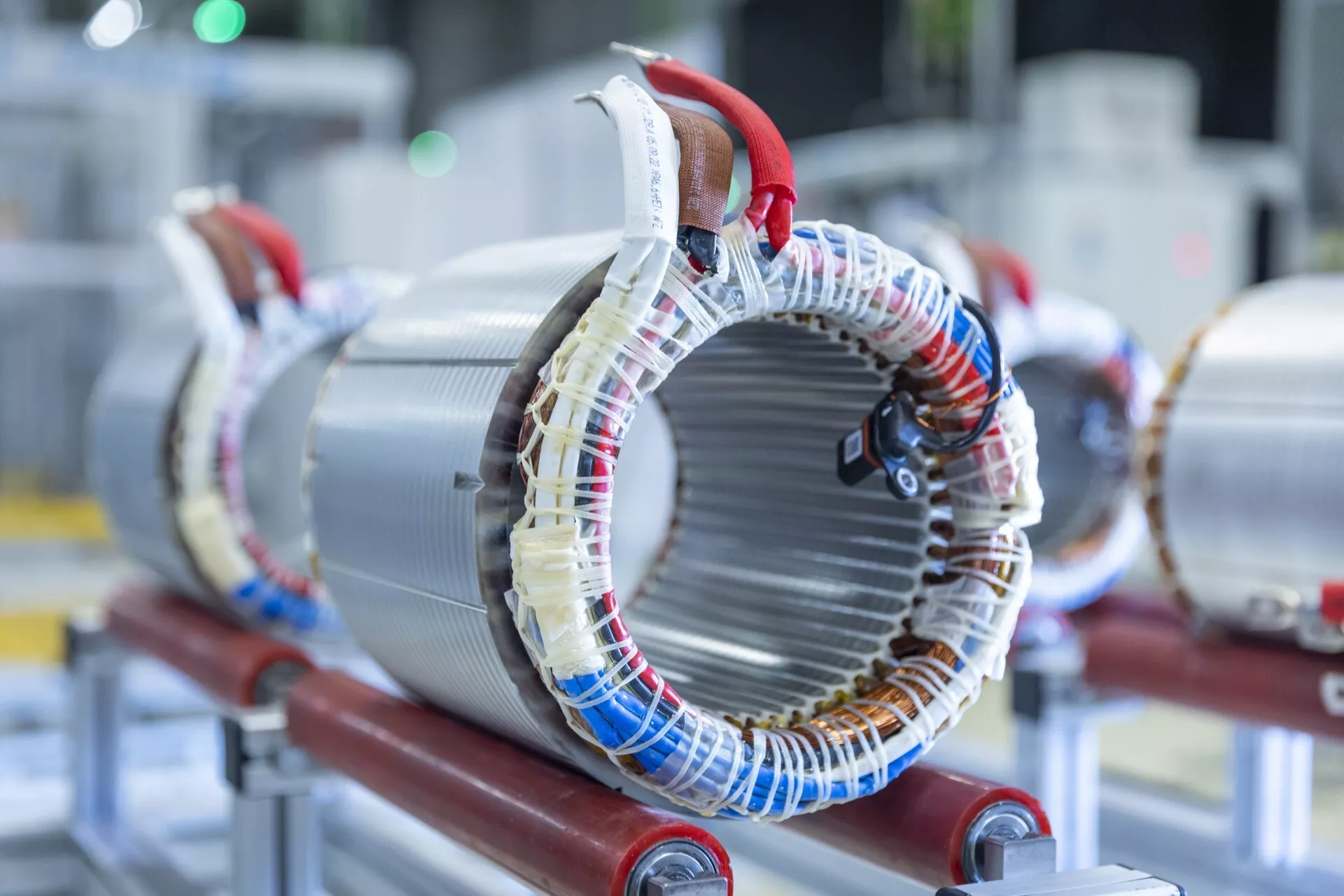 Magas felbontású fénykép egy vörös tartón felszerelt elektromos motor állórészéről, amely ábrázolja a mágneses mezők előállításához elektromos gépekben tipikus, laminált fém magok köré tekert dróttekercseket