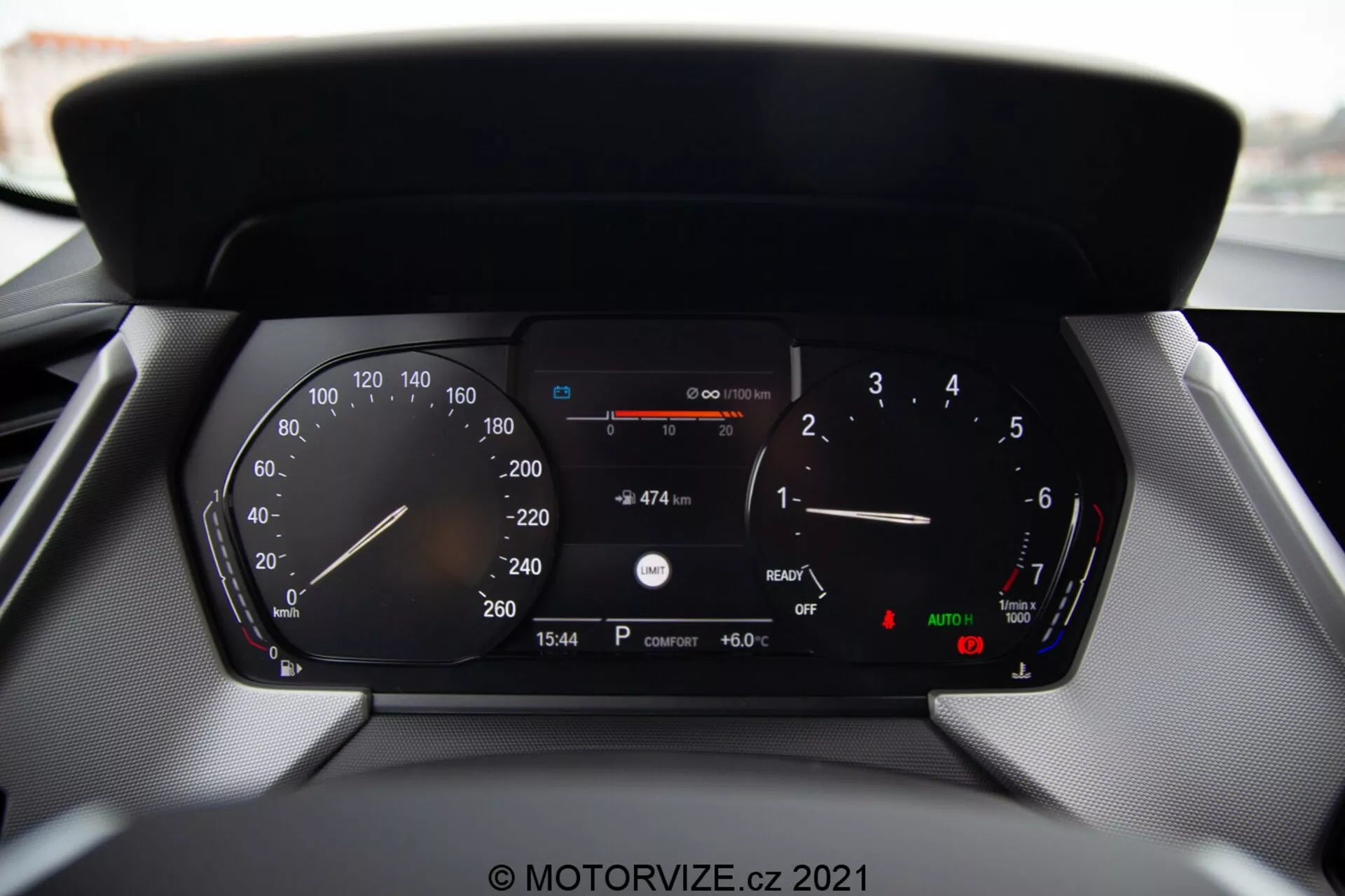 Közelkép egy modern autó digitális műszerfaláról, egy BMW 1-es sorozat 2019-es modelljéről (BMW 116i), részletes kijelzésekkel, beleértve a sebességmérőt, a fordulatszámmérőt, az üzemanyagszint-mérőt, a hőmérsékletmérőt, a digitális sebességmérőt, az aktuális üzemanyaggal megtehető távolságot, az időt (15:54), a külső hőmérsékletet (6.0°C) és az automatikus fényszórók, valamint a kézifék jelzéseit.