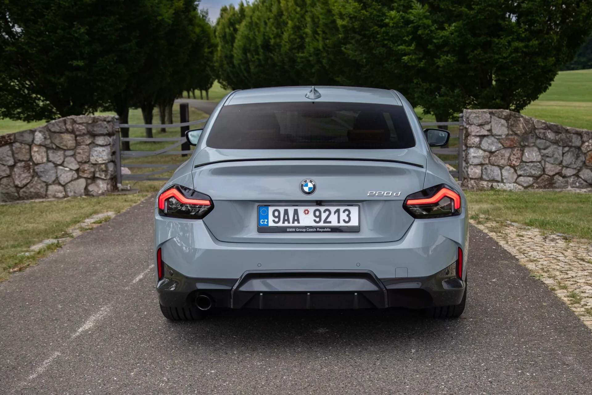 Hátsó nézet egy szürke BMW M3 szedánról (G80 modell), melyen jól látható a BMW embléma, az M3 és a G80 modellmegjelölés, a központi rendszámtábla, a sportos hátsó lökhárító beépített diffúzorral, szimmetrikusan elhelyezkedő dupla kipufogóvégekkel, teljes szélességű L-alakú LED hátsó lámpák és a kiszélesített kerékjárati ívek.