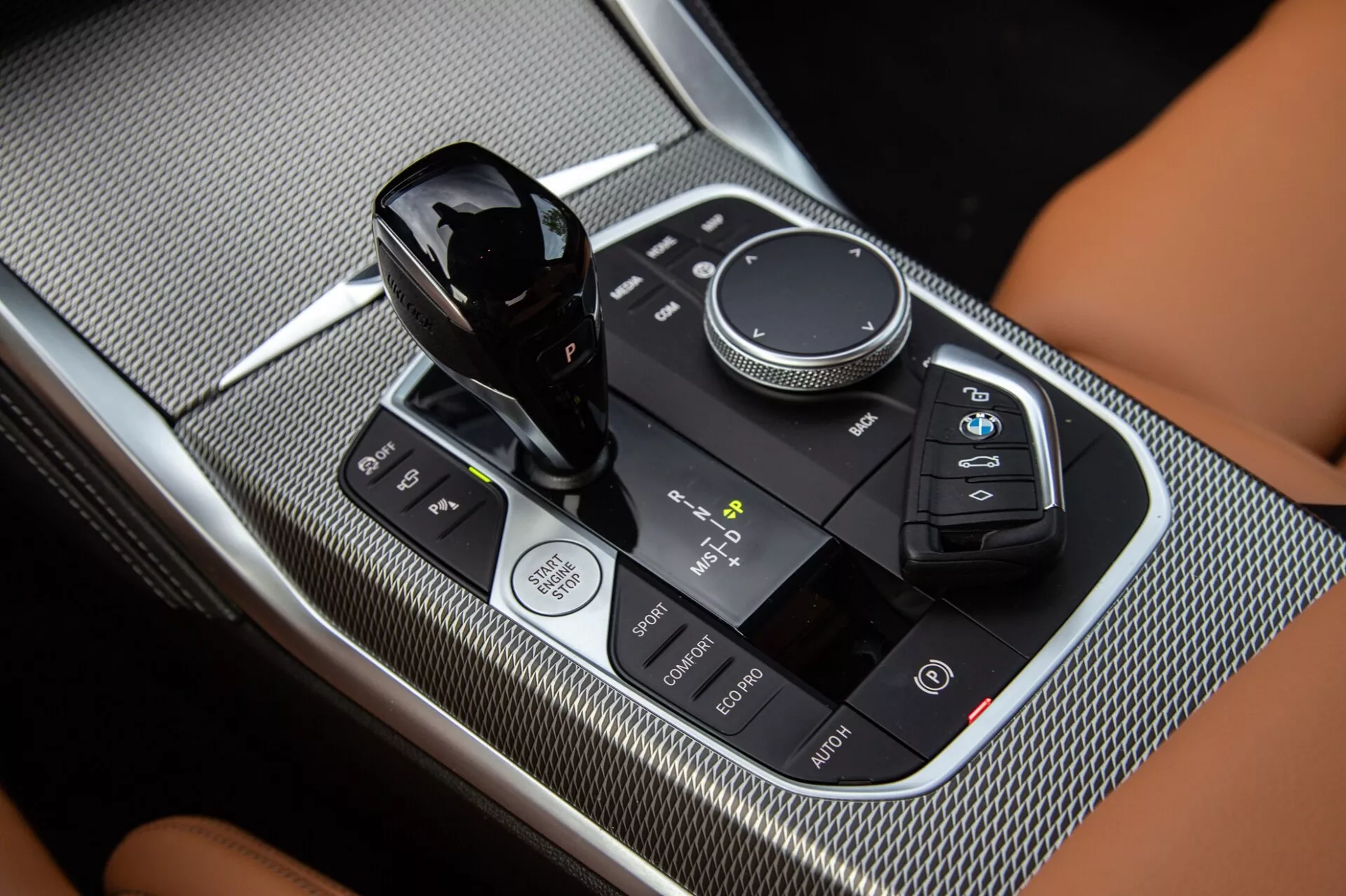 Közelkép a BMW 2-es sorozat Coupé 2022 középkonzoljáról, kiemelve a sebességváltó kart, a multimédiás vezérlőtárcsát és az érintőpanelt fényes fekete és szénszálas textúrájú felületekkel.