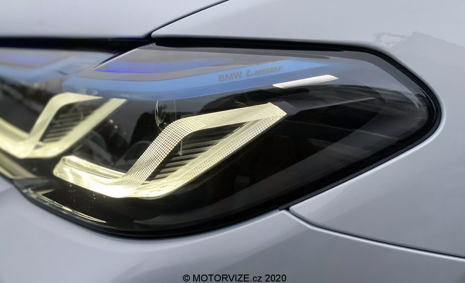 A 2020-as BMW 520i Touring Steptronic első bal fényszórójának közeli képe, amely bemutatja az elegáns, ívelt polikarbonát lencseburkolatot, a jellegzetes dupla hélix formájú LED nappali menetfényeket, a fényvisszaverő burkolatot és a 'BMW Laser' feliratot, kiemelve az előrehaladott lézer fénytechnológiát és a prémium minőségű fémes karosszériapanelt.