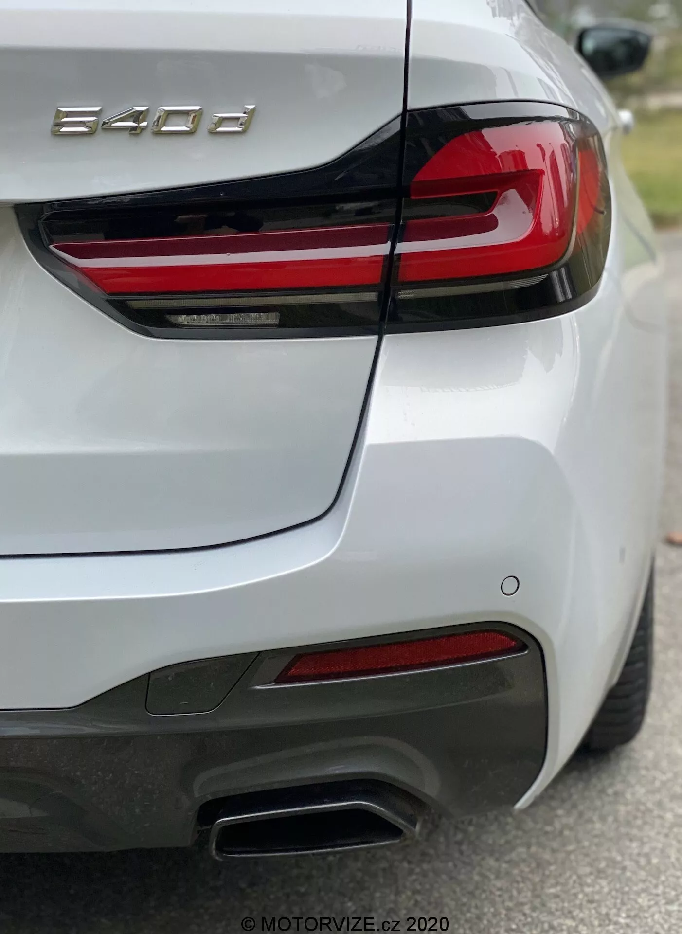 BMW 8-as sorozat (840i) személyautó hátsó része, amelyet jobb hátsó negyed nézetből rögzítettek, kiemelve a jobb hátsó lámpát vízszintes piros LED csíkokkal, a formázott csomagtérfedelet beépített spoilerral, a hátsó lökhárítót szenzorokkal, dupla fém kipufogóvégeket a jobb oldalon, piros fényvisszaverőket és fényes fehér fényezést. A fotó az '840i' jelvényre összpontosítva mutatja a részletes tervezési elemeket és a technológiai jellemzőket, mint például a világítást és a vezetőtámogató rendszereket.