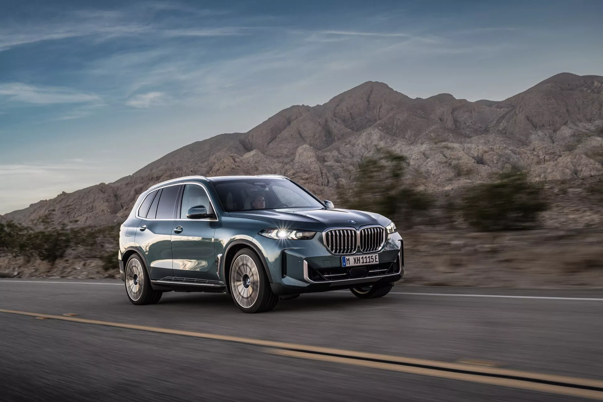2023-as BMW X5 (G05-F95 Facelift) modern luxus SUV mozgásban, háromnegyedes első nézetből kiemelve a dinamikus tervezést, nagy vese alakú hűtőrácsot, karcsú LED fényszórókat, többsugaras ötvözött kerekeket és sima sziluettet metalikus festéssel