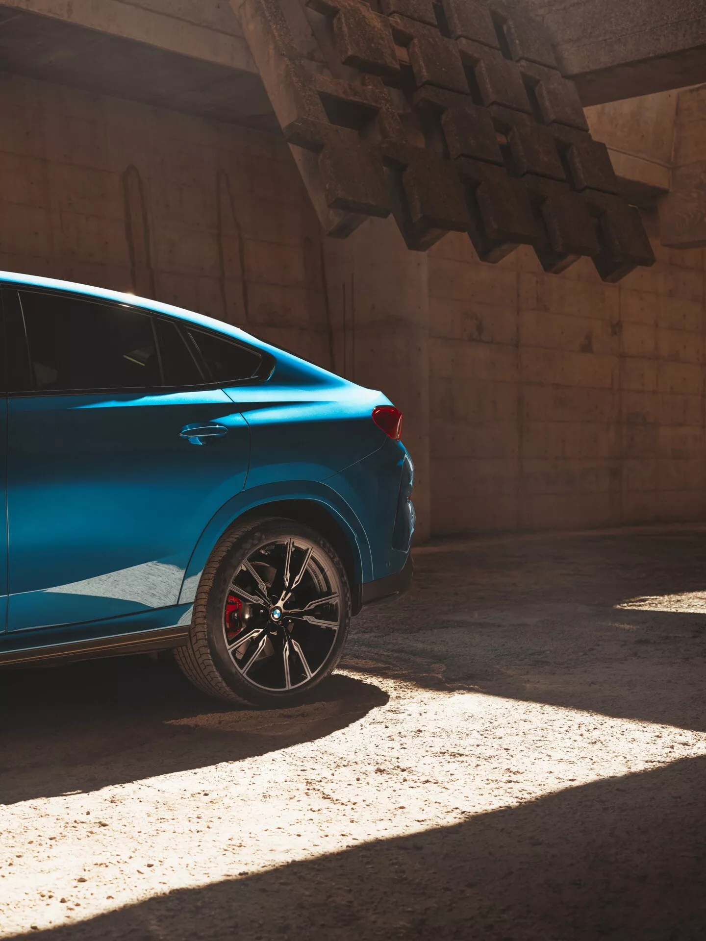 2023-as kék BMW X6 (G06/F96 felújítás) napfényben, hátulról háromnegyedes nézetben, a hátsó negyedet hangsúlyozva sportos felnivel és piros féknyergekkel.