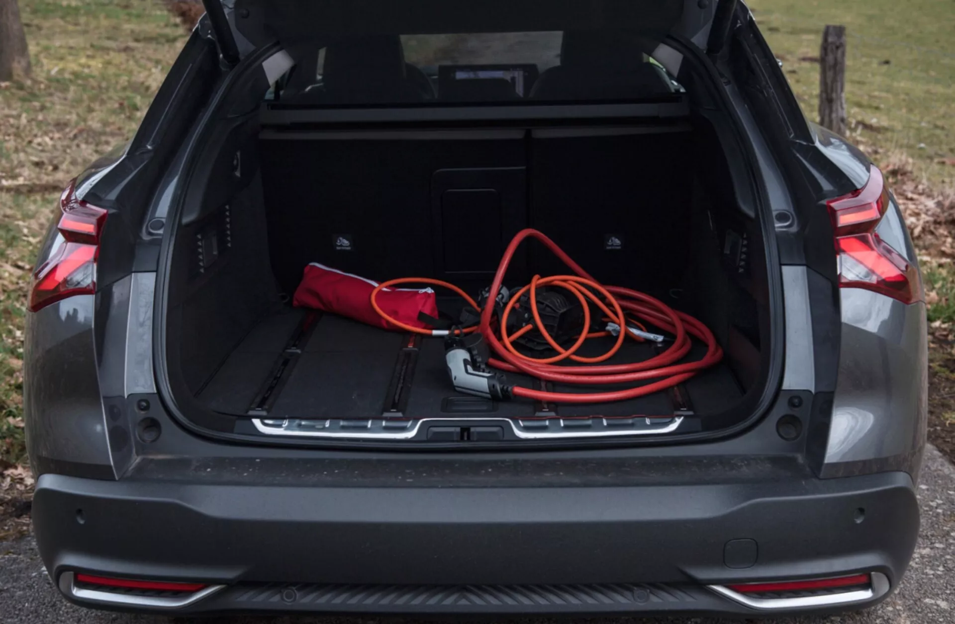 2022-es Citroen C5-X hátsó csomagterének térképe az nyitott rekesz megjelenítésével, tágas rakodóterülettel, piros-fekete táskával, narancssárga hosszabbítóval, további tárolóhelyekkel, védőléccel és parkolóérzékelőkkel, természetes kültéri fényben