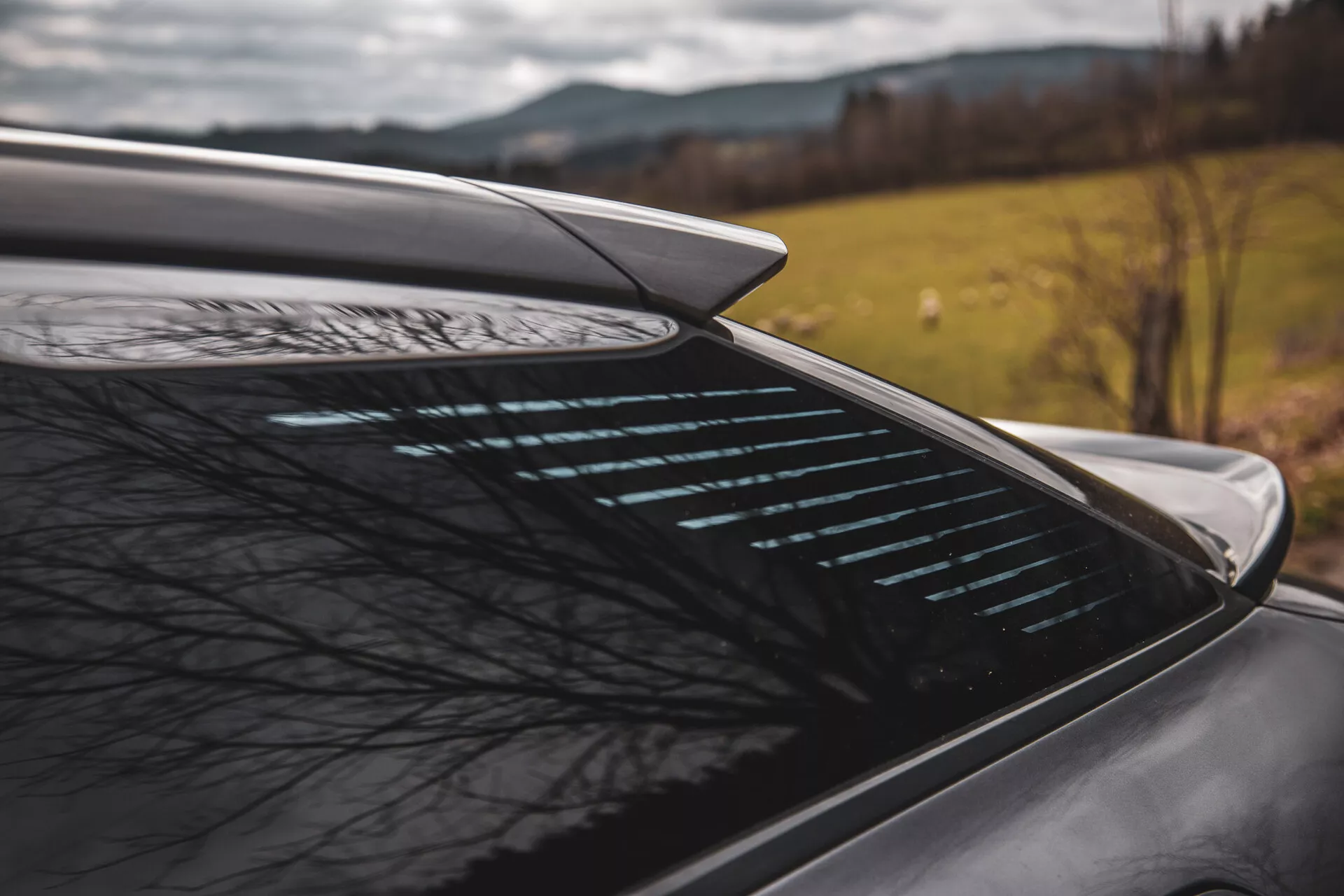 Közeli oldalsó nézet a Citroen C5-X 2022 hátsó részére integrált aerodinamikai spoilerrel és leolvasztó hátsó ablakkal homályos természeti háttérrel szemben, ami a jármű teljesítményét és biztonsági jellemzőit sugallja egy lehetséges vidéki környezetben