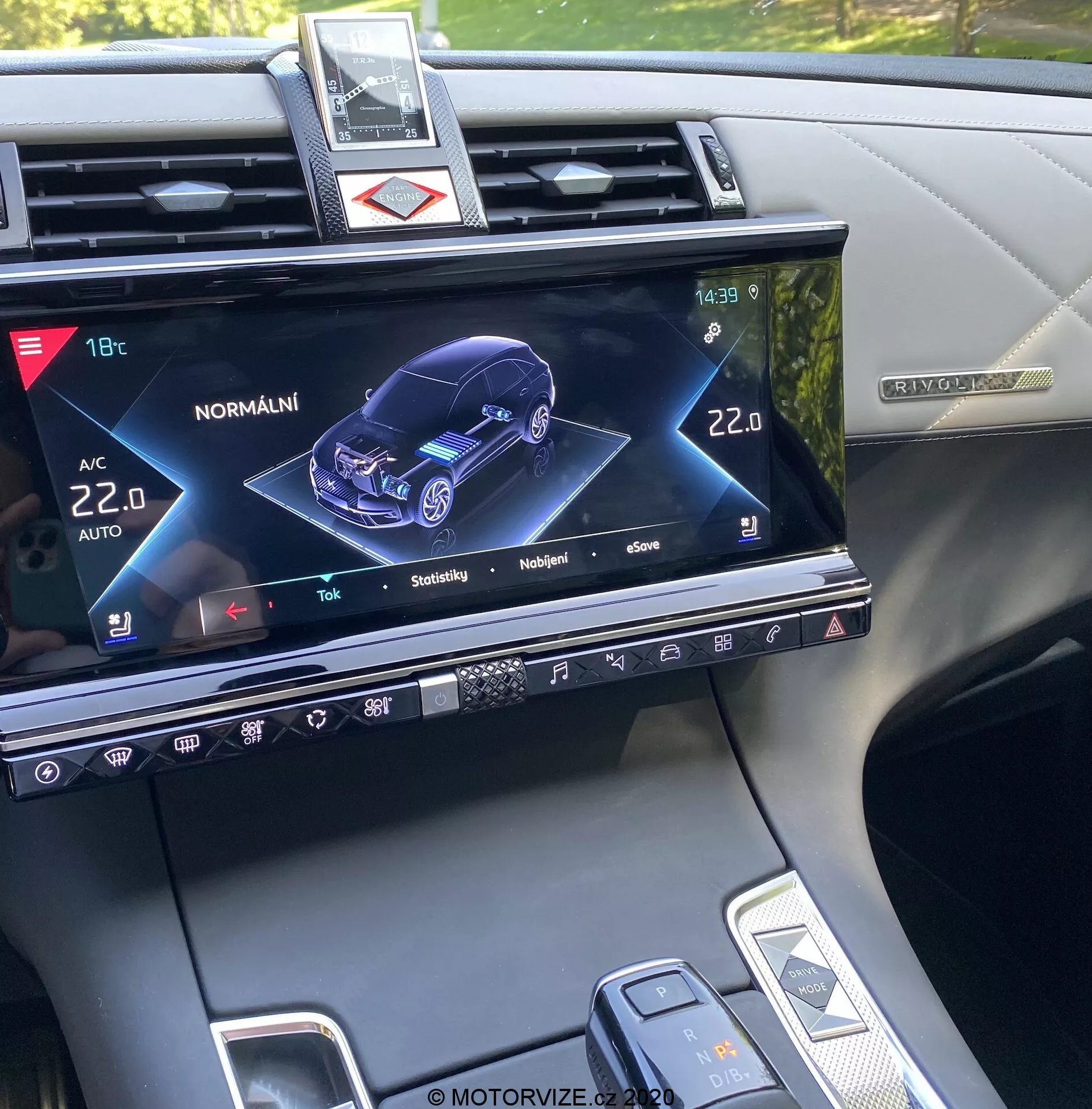 A 2018-as DS Automobiles DS-7 Crossback középkonzolja, amely az infotainment rendszer kijelzőjét mutatja, egy 3D-s grafikus ábrázolással a jármű elülső-jobb perspektívájából, jelezve annak állapotát és különféle beállításait, mint például a klímavezérlés, az ülésfűtés, valamint az autómodell interaktív funkciói, fizikai gombokkal, érintésérzékeny vezérlőkkel és a váltókar és a jármű beállító tárcsa részleges nézetével.