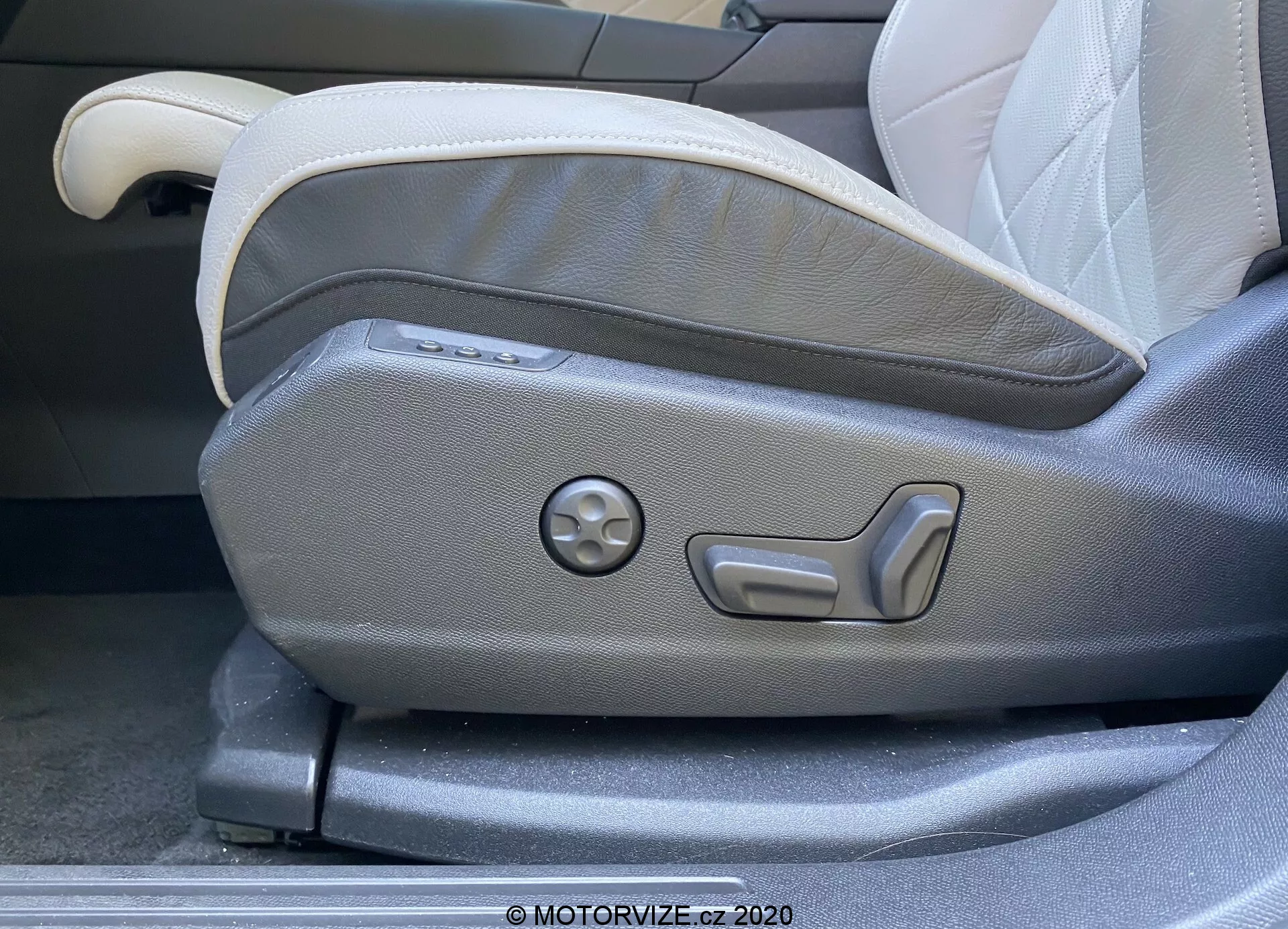 Közelkép egy 2018-as DS Automobiles DS 7 Crossback vezetőoldali első ülésének állítópaneljéről. A kép elkapja az elektromosan működtetett ülésállító gombokat, beleértve a többszintű állíthatóságot és egy kerek tárcsát a memóriabeállításokhoz. Az ülés két tónusú kárpitozással rendelkezik világos és sötétszürke színekben, modern, ergonomikus dizájnt mutatva, amely jellemző a luxus autó belső terekre.