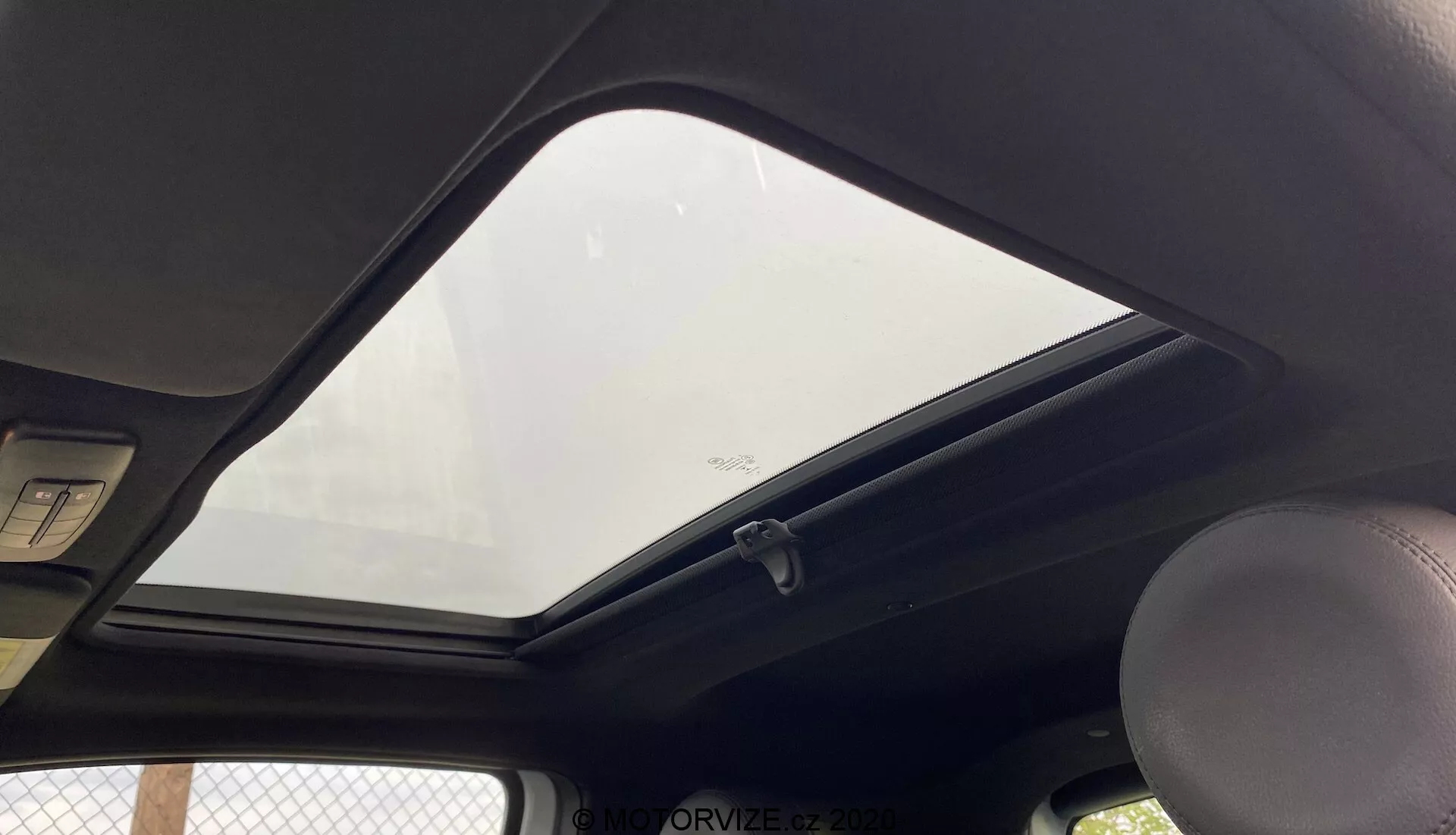 A 2015-ös Fiat 500 belső nézete a tető felé fókuszálva, egy utas vagy vezető perspektívájából. A zárt napfénytető lehetővé teszi a természetes fény beáramlását az utastérbe. A sötét színű tetőkárpit kontrasztot alkot a külsejével. Látható kapaszkodó a bal oldalon, egy standard kupola világítás fölötte és két napellenző szélei felül. Ruhafogas a napfénytető üvegének szélénél, az alsó részen egy biztonsági címke látható. A kép alacsony szögből készült, közelről keretezve a belső tető jellemzőit.