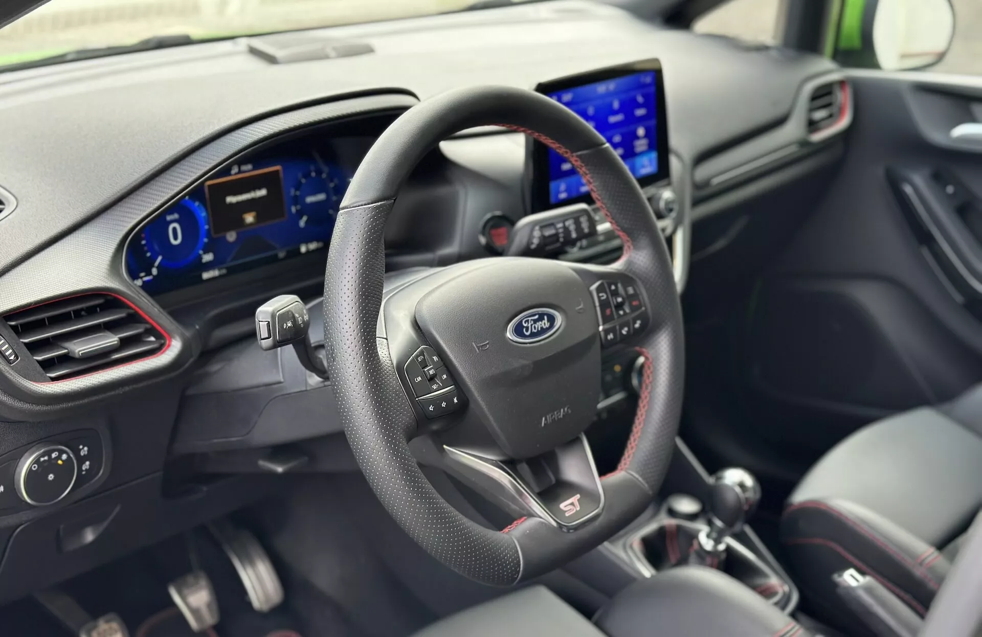 2022-es Ford Fiesta belső tér a vezető perspektívájából, bőr kormánykerék vezérlőgombokkal, Ford logó, digitális műszerfal és modern infotainment rendszerrel a műszerfalon