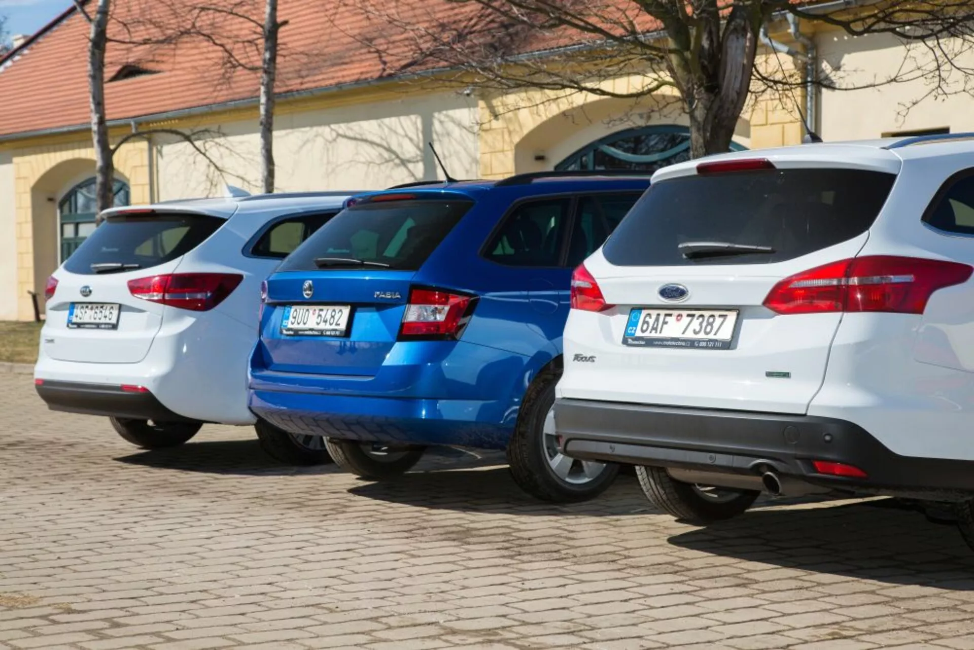 Három ferdehátú sorakozik, beleértve egy 2011-es fehér Ford Focust is, merőlegesen parkolva a hátsó végekkel a kamera felé fordulva, bemutatva a hátsó lámpákat és a hátsó rész dizájnjellemzőit egy jól megvilágított parkolóterületen.