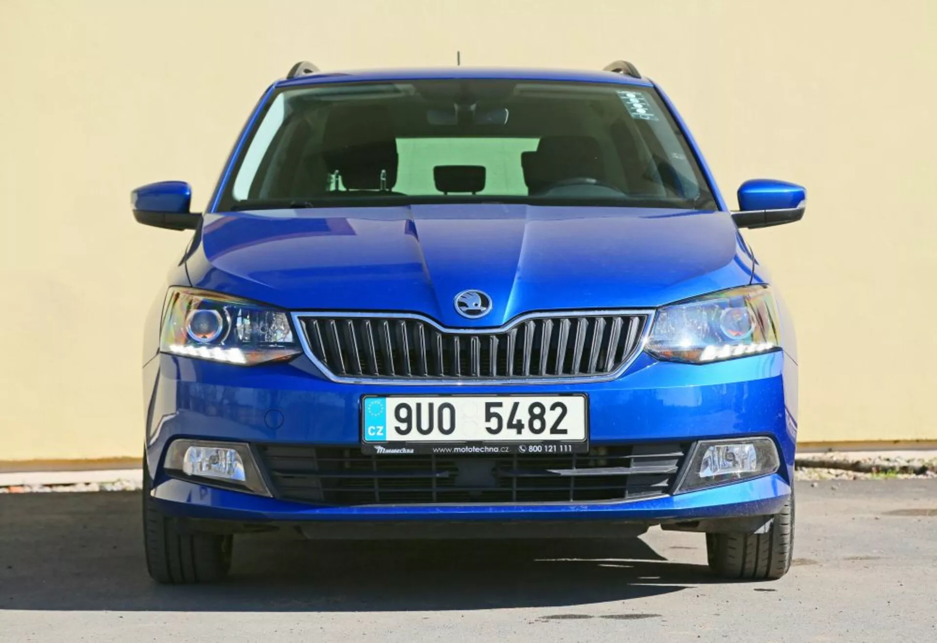 Kék Škoda jármű elölnézeti képe, amelyen a márkajelzés a krómozott hűtőrács közepén, tiszta lencsés fényszórók és fekete házban elhelyezkedő ködlámpák láthatók, részletes alsó hűtőráccsal és faragott motorháztető tervezéssel.