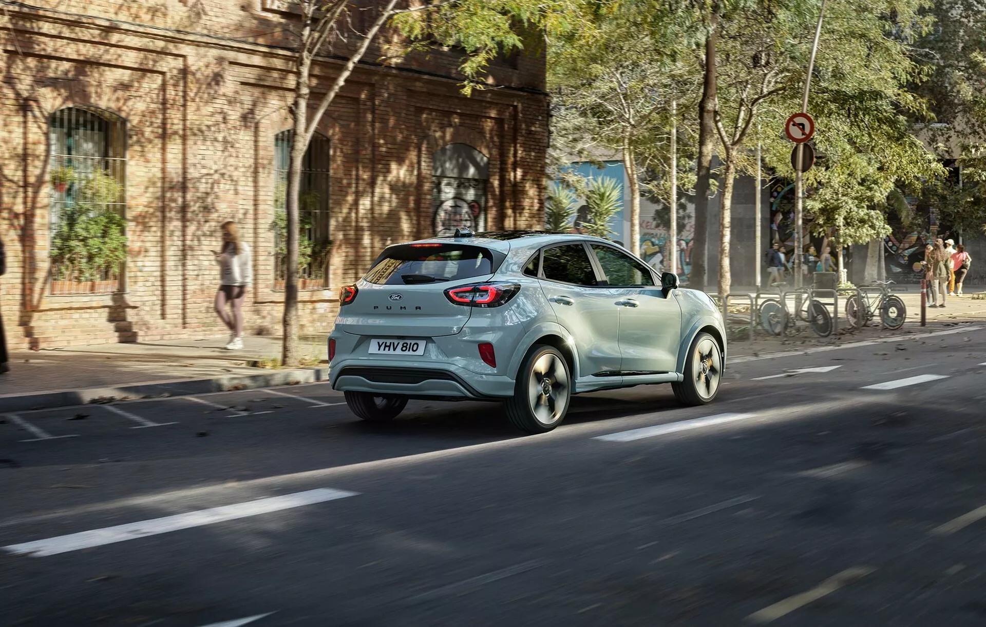 2024-es Ford Puma (II-facelift) világosszínű ferdehátú mozgásban egy városi utcán háromnegyedes hátsó szögből megmutatva a hátsó lámpákat, a hátsó ablakot, az oldalajtókat és az ötvözött kerekeket