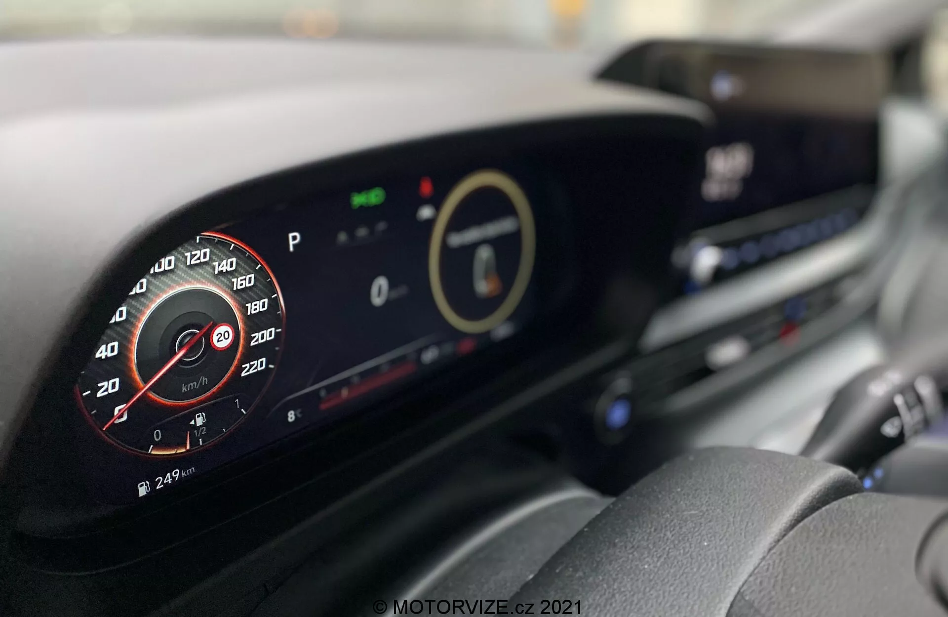 Hyundai i20 2020 belső tere modern műszerfallal. Kép a vezető üléséből, amely a digitális műszerfalra és a központi kijelzőre összpontosít, részleteket mutat, mint például a szimulált analóg fordulatszámmérő, környezetbarát jelzők és az infotainment rendszer. További látható jellemzők a légbeömlők és a klímavezérlő gombok.