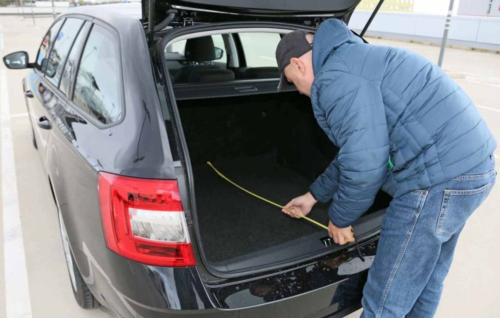 Hyundai i30 2017 (i30-N) bemutatja a tágas csomagtartóját, amely szövettel borított belsővel rendelkezik, modern LED hátsó lámpákkal és egy személlyel, aki méri a csomagtartó terét, háromnegyed nézetből napfényben, a szabadban