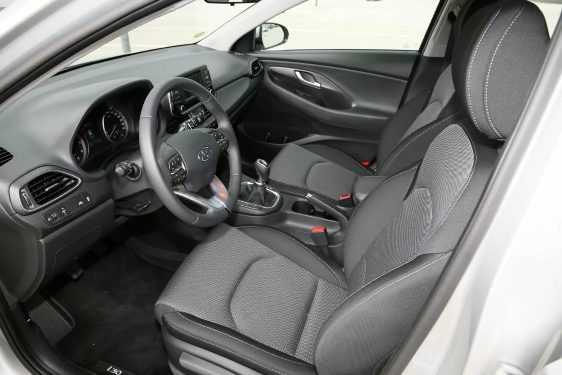 Hyundai i30 2017 (i30-N) belső nézete, ahol a fókusz az első utastérre irányul, bemutatva a vezetőülést kormányon elhelyezkedő vezérlőkkel, kézi váltóval, középkonzollal és mintás szövet ülésekkel